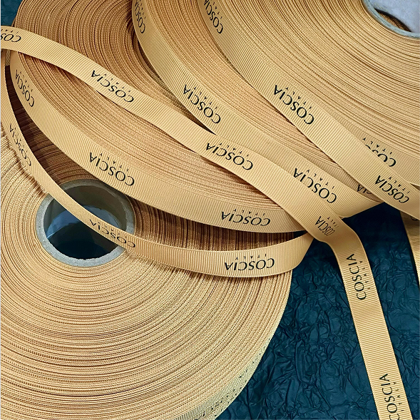 Rolls of warm amber custom printed COSCIA grosgrain ribbon