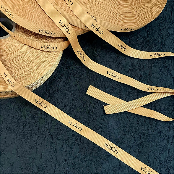 Loose warm amber grosgrain ribbon rolls with repeated COSCIA logo printing