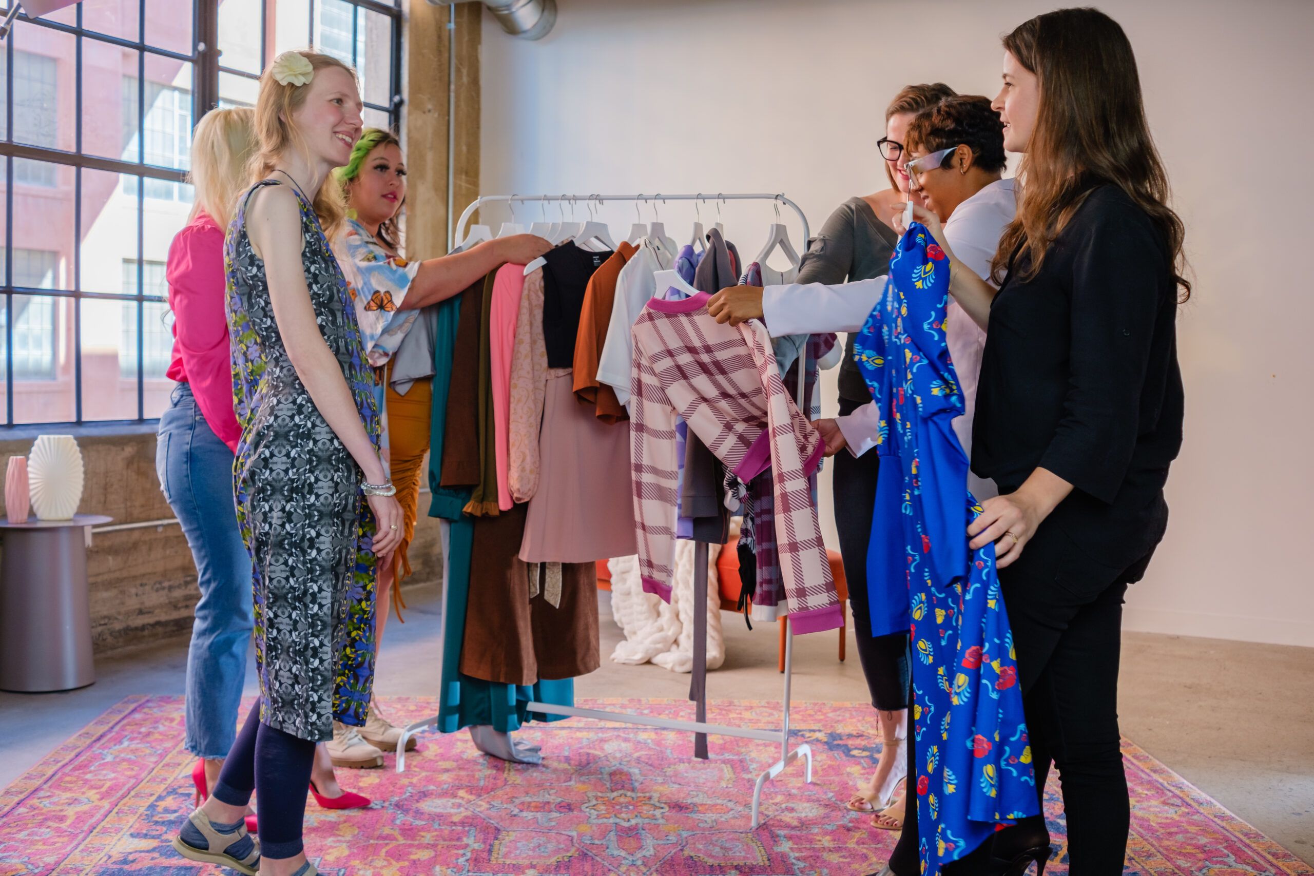 People are looking at clothes on a rack in a bright room