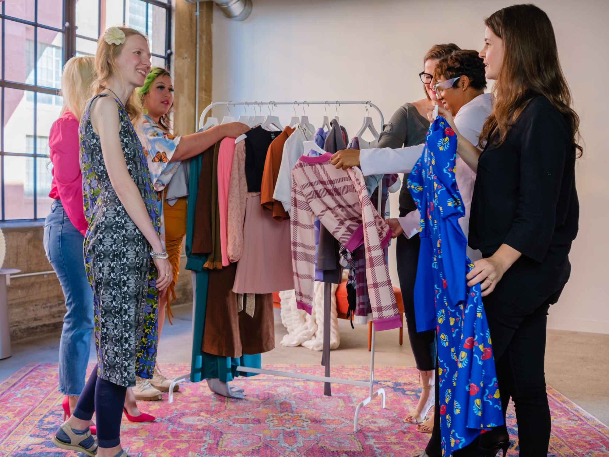 People are looking at clothes on a rack in a bright room