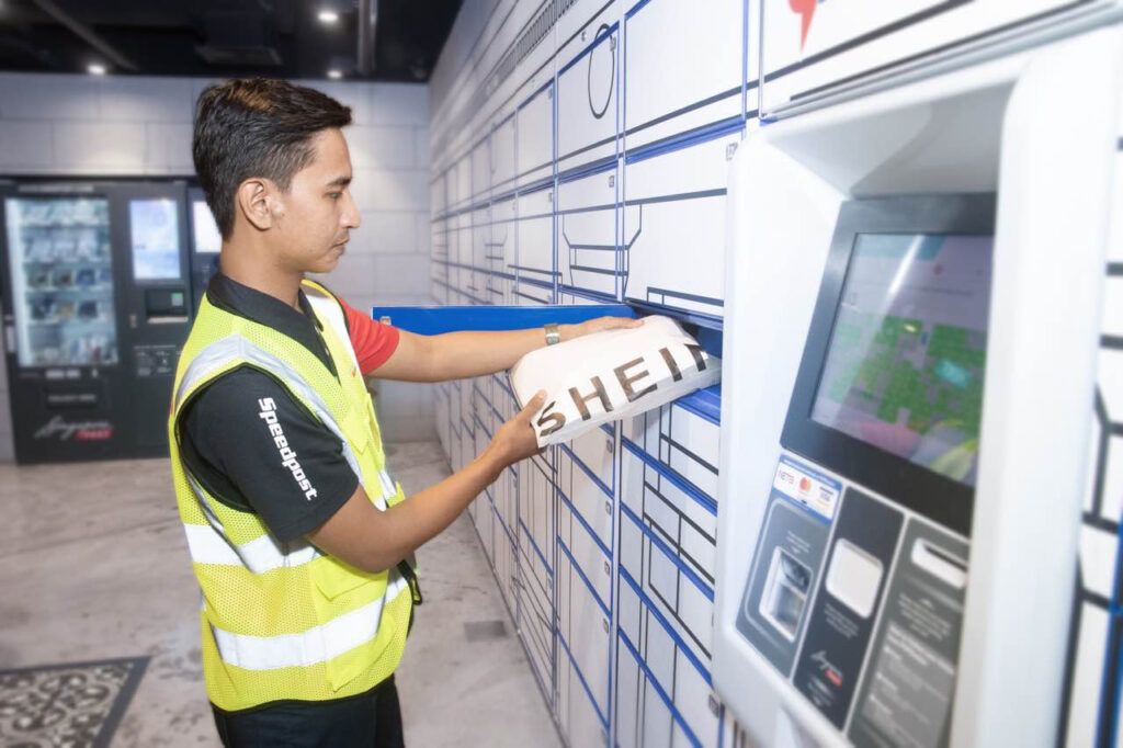 A worker in a Speedpost vest is placing a SHEIN package into a parcel locker system