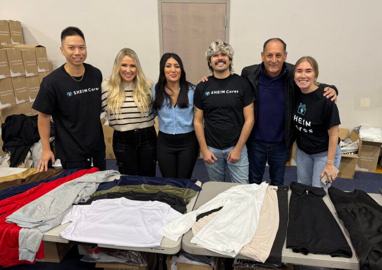 Six people posing in front of a table with clothes