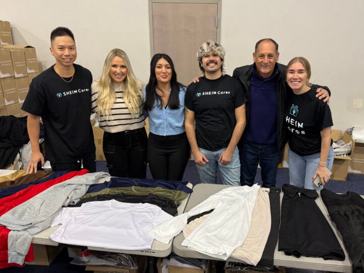 Six people posing in front of a table with clothes