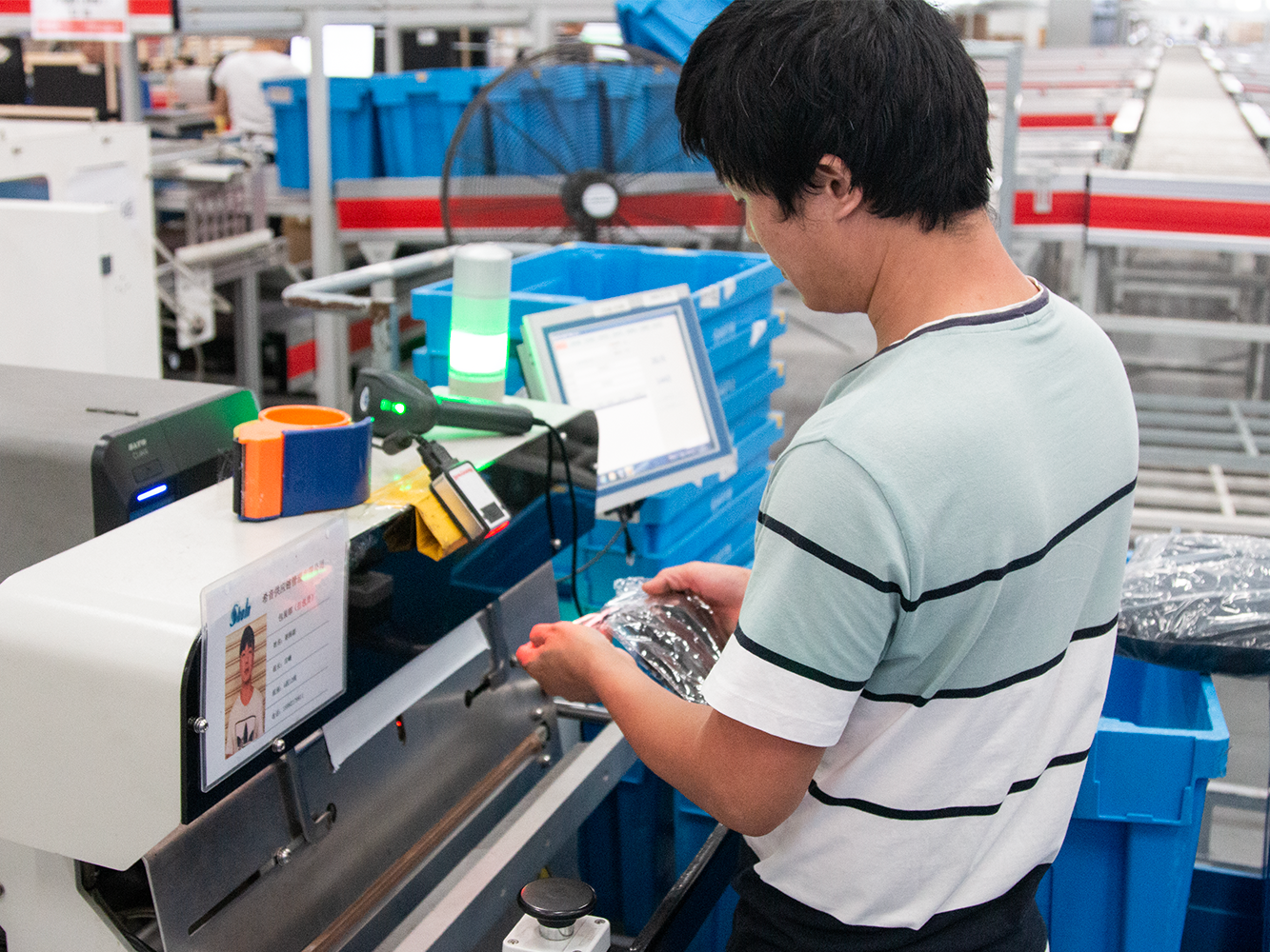 Warehouse worker scanning and packaging products at a workstation with blue storage bins and computer display