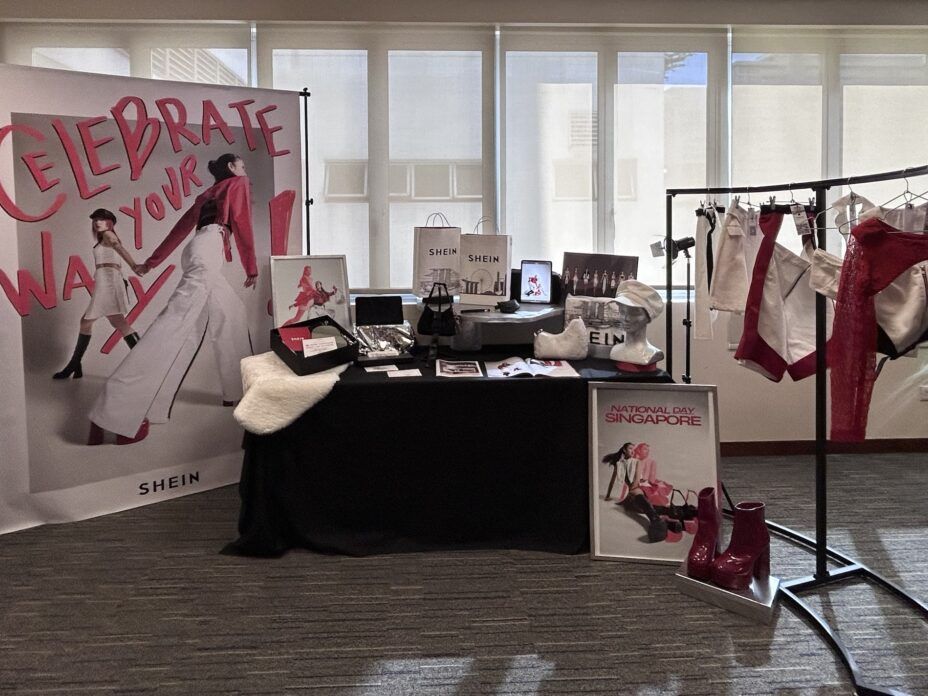 A SHEIN display features a banner, table with accessories, and clothing on a rack indoors