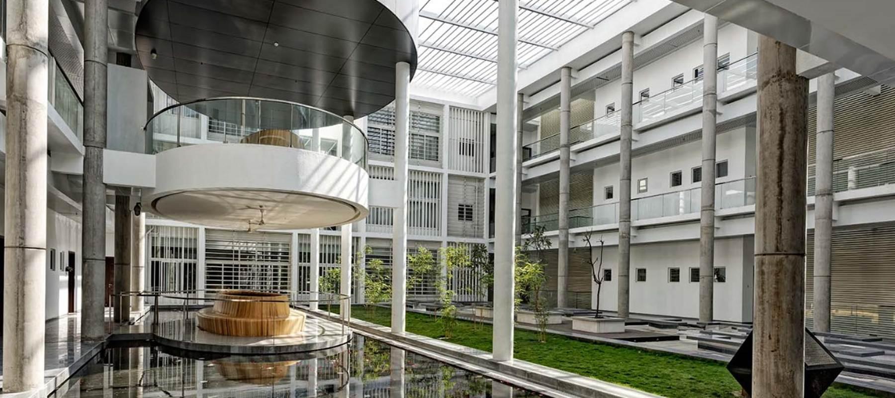 VVIP Circuit House, Pune: daylit atrium with a suspended circular gallery above a reflecting pool and courtyard lawn