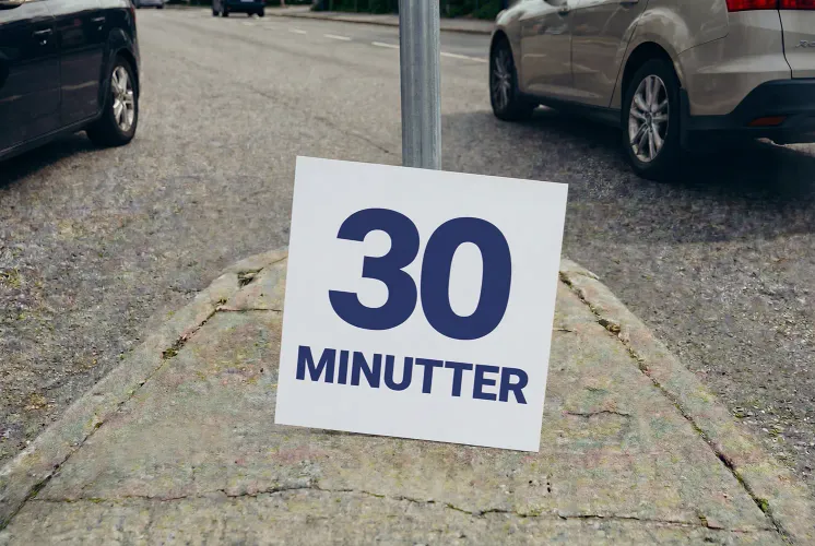 Et skilt med teksten '30 minutter' i en midtrabatt med biler på hver side.