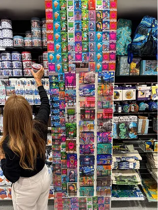 Shopper reaching for a 3D postcard on a tall Orange Panda display in a souvenir shop