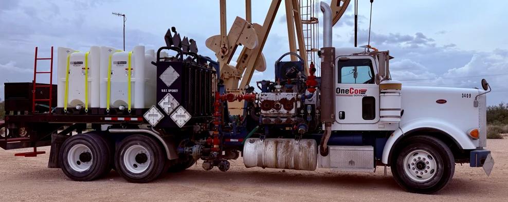 OneCor 600 HP acid pumper with chemical tanks, parked beside a pumpjack