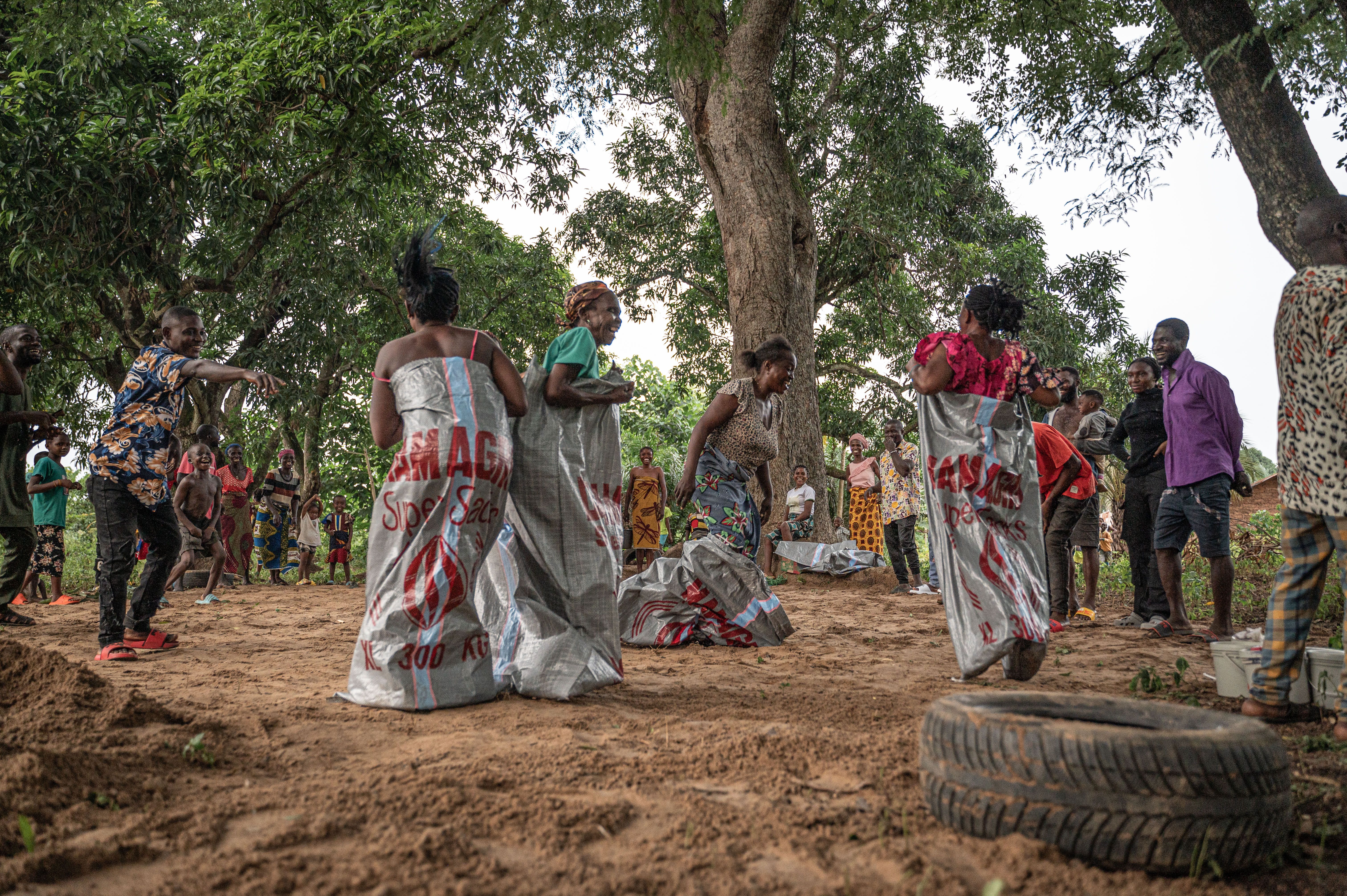Women laughing while competing in a sack race with community members cheering in the background
