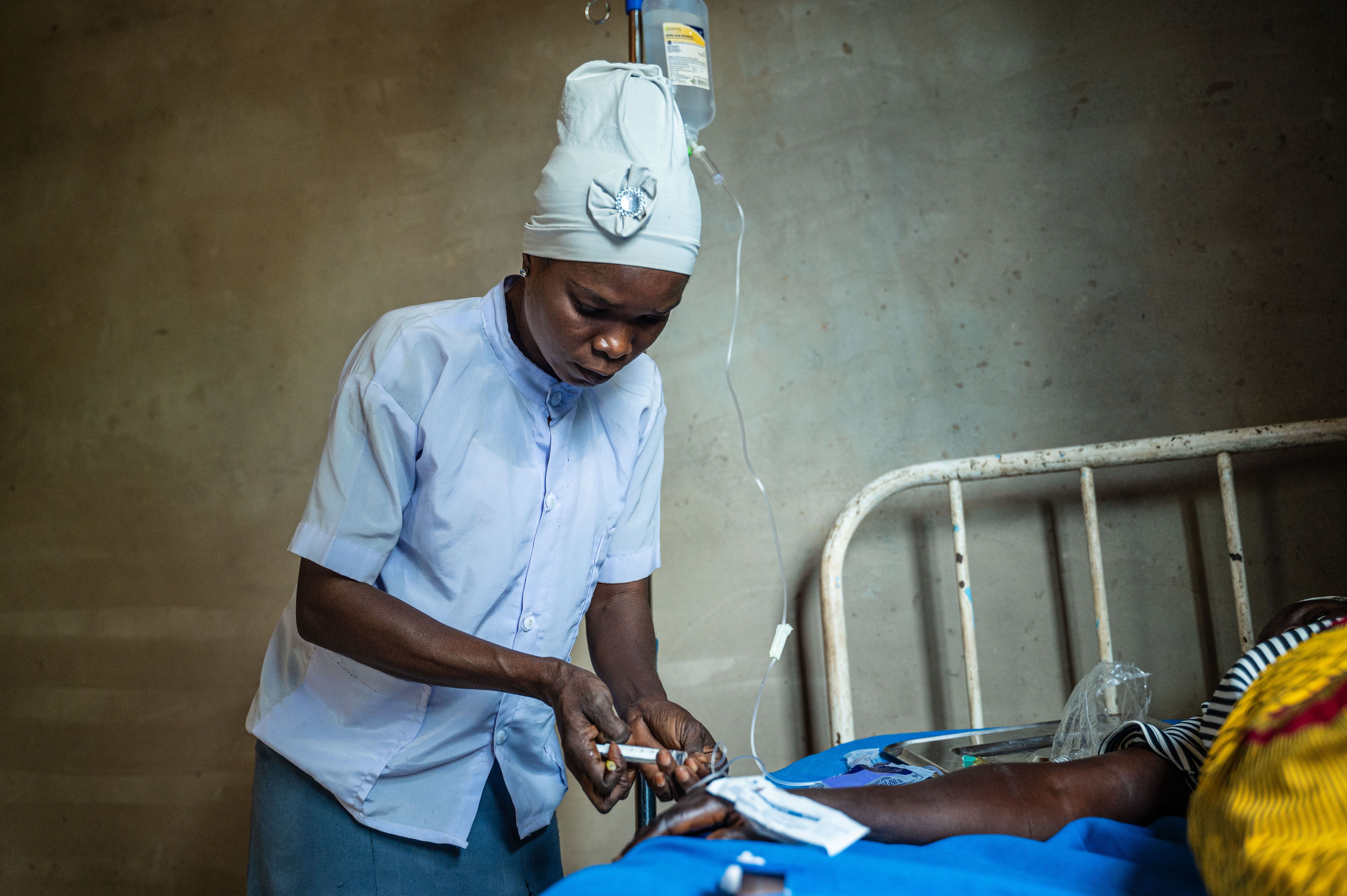 A nurse adjusting an IV line for a pregnant woman lying on a bed in a rural clinic.