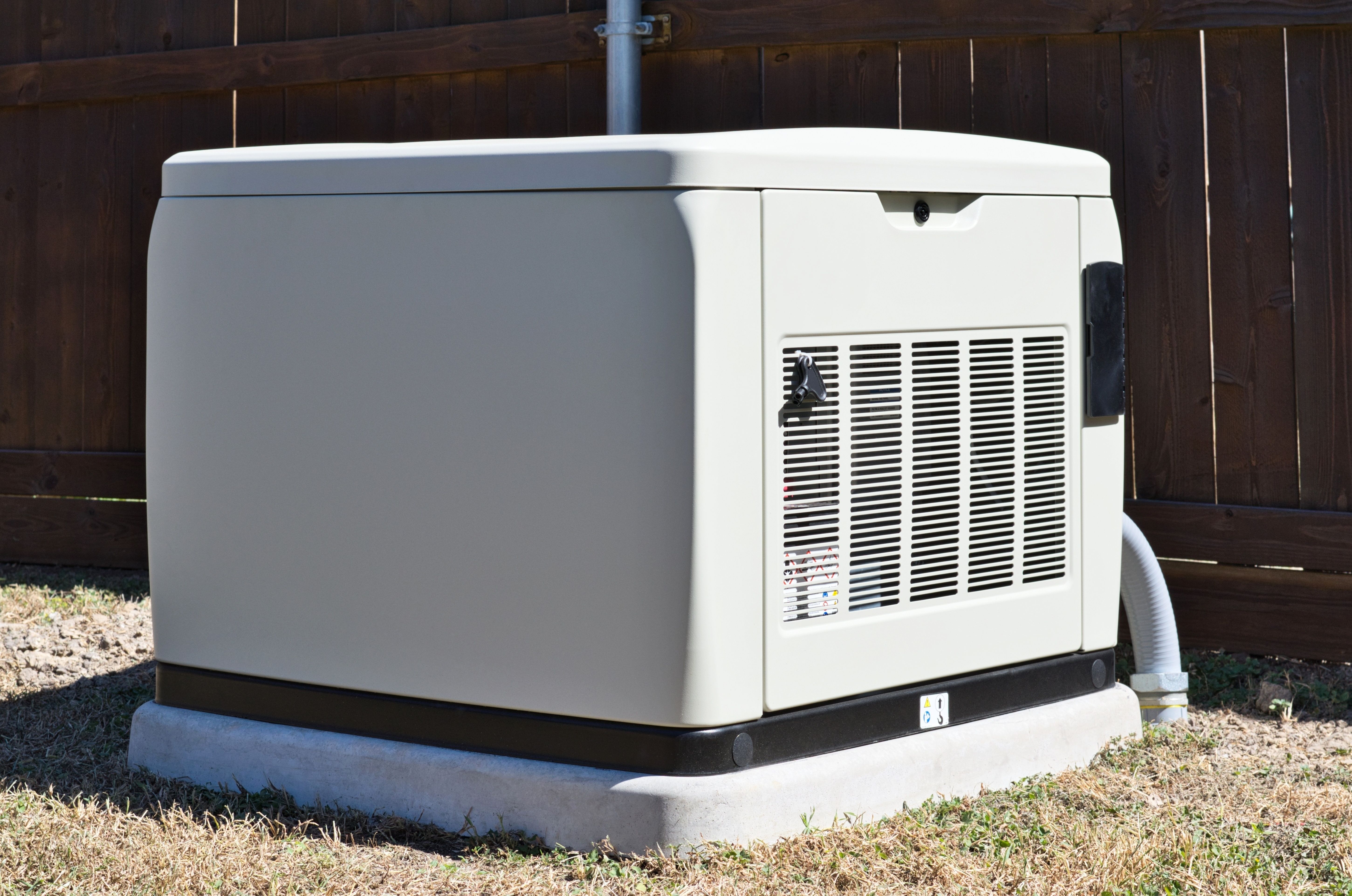 A whole-home standby generator installed on a concrete pad beside a wooden backyard fence.