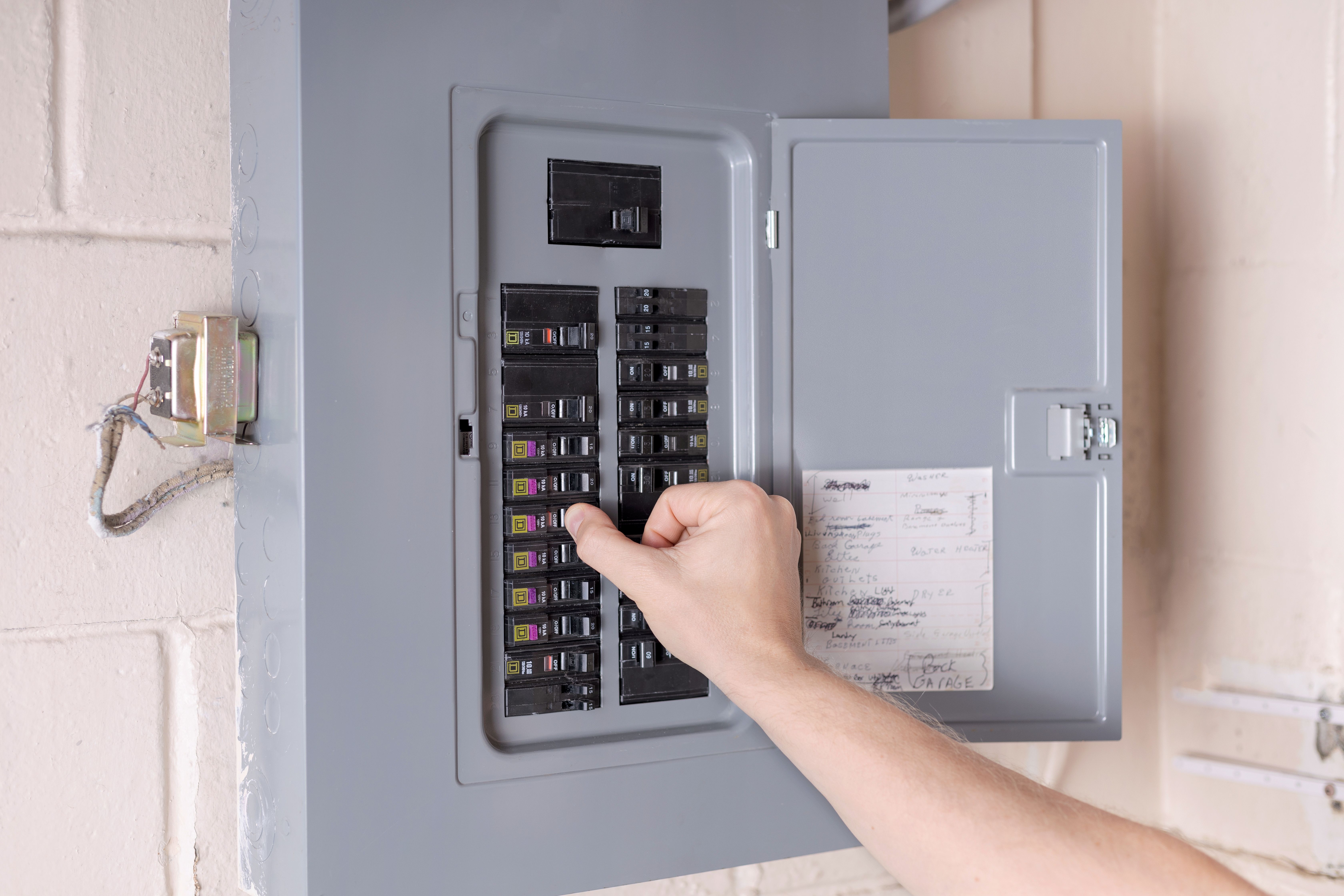 A hand reaching into an open residential electrical panel to reset a breaker, beside a handwritten circuit directory.