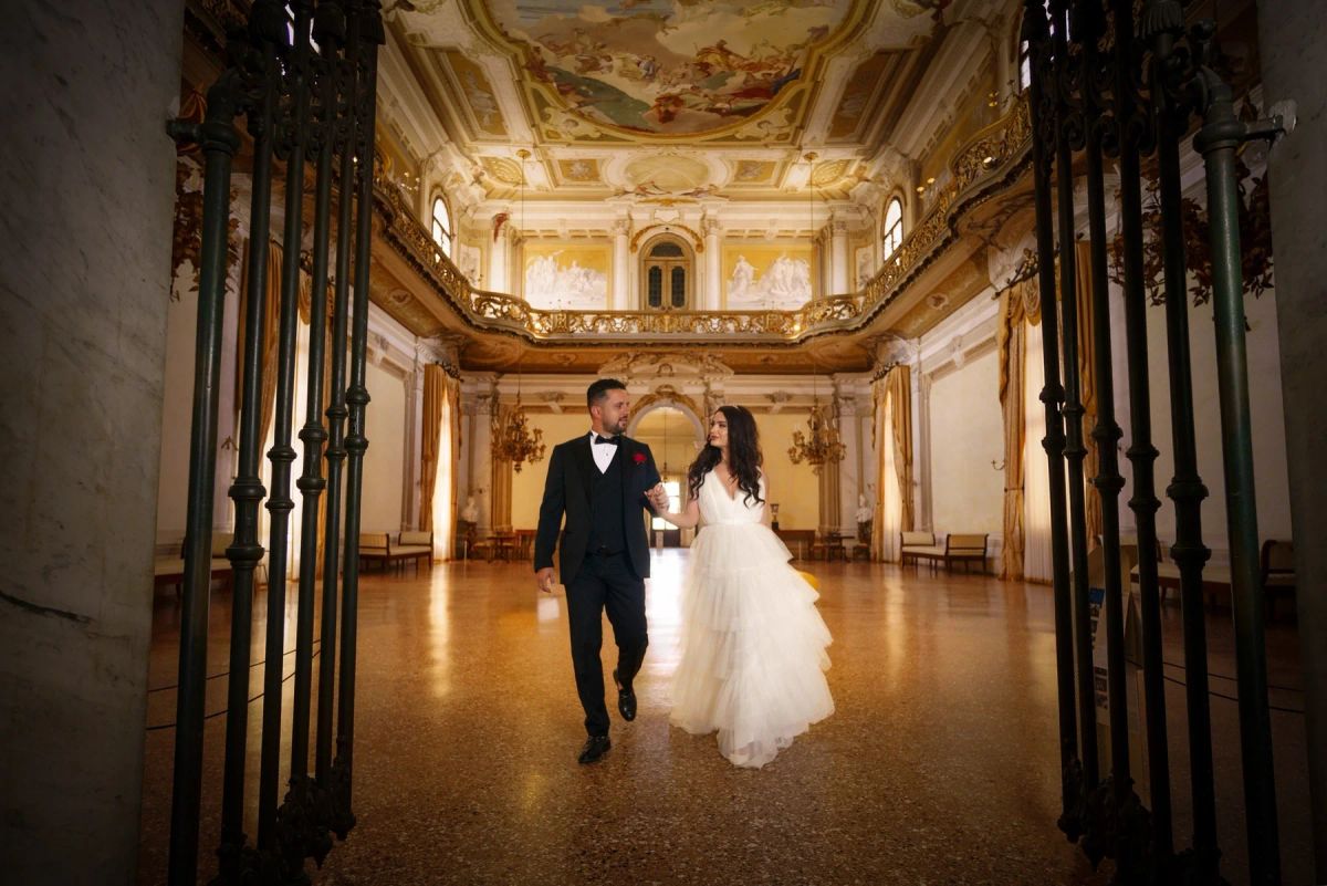 Editorial wedding couple walking through a grand historic interior — photograph by Ergys Shehu.