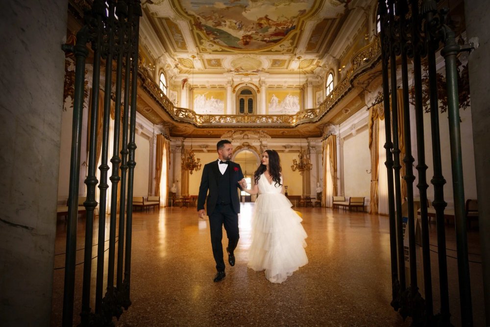 Editorial wedding couple walking through a grand historic interior — photograph by Ergys Shehu.