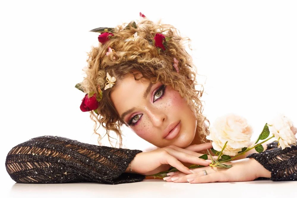Editorial beauty portrait with sculptural curls, flowers and a clean white setting — photograph by Ergys Shehu.