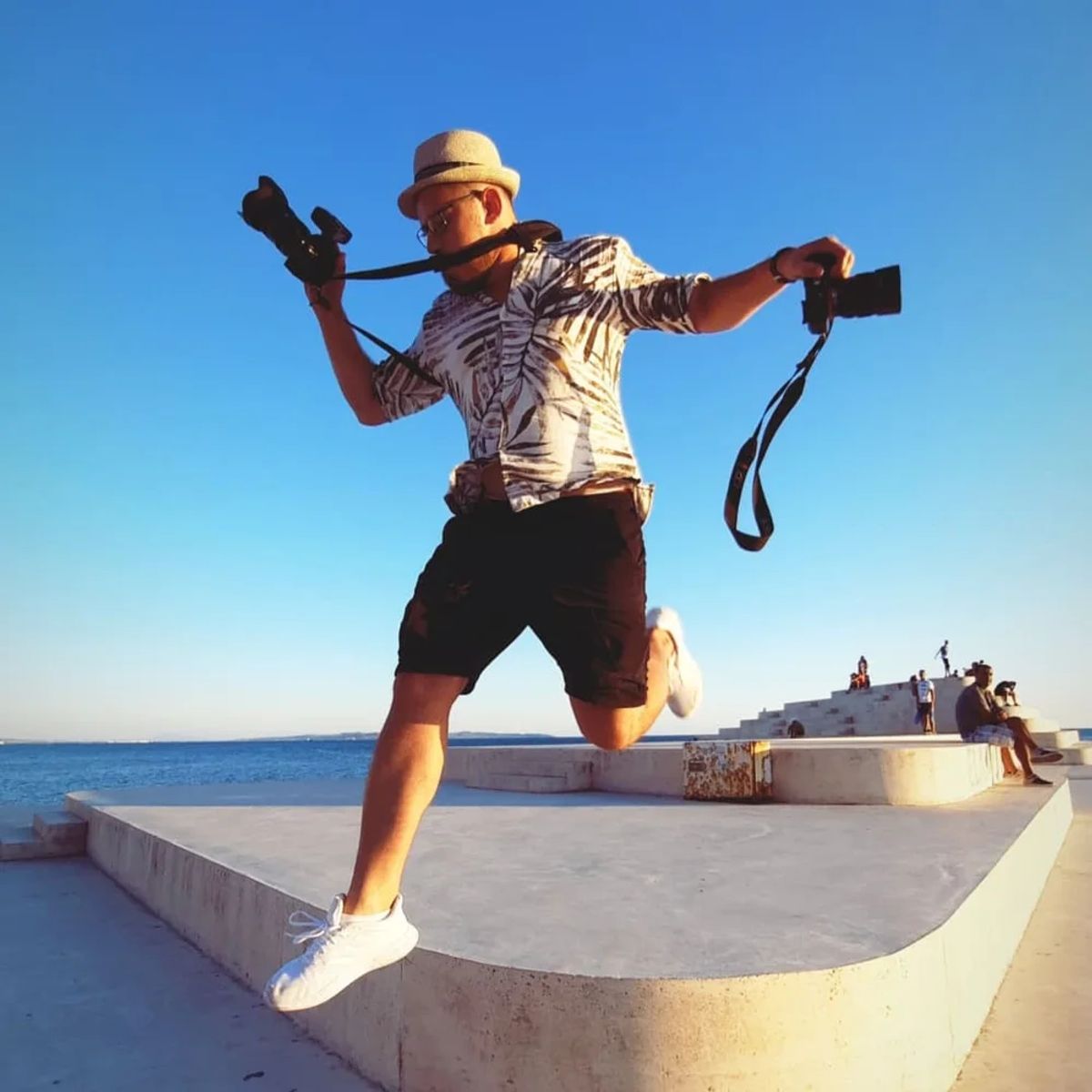 Ergys Shehu jumping mid-air with two cameras by the sea