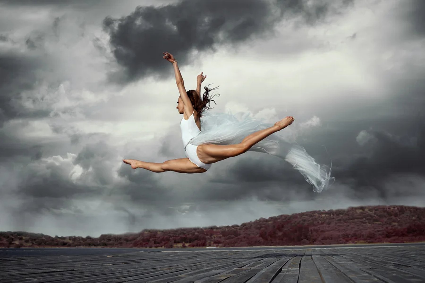 A dancer suspended mid-leap against a dramatic sky