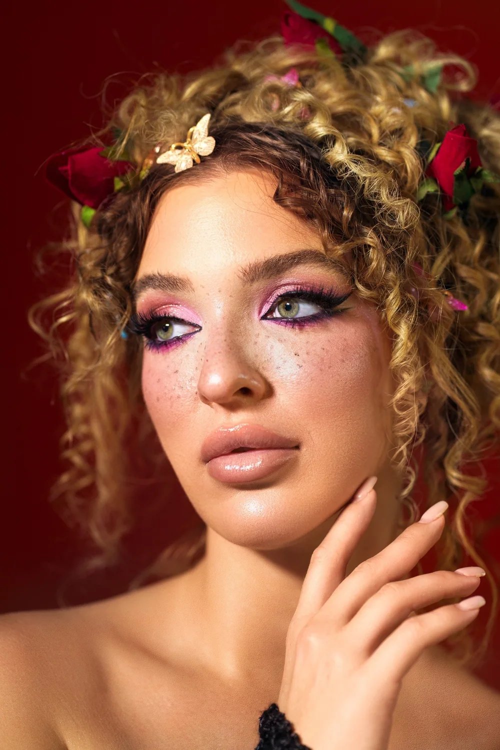 Close editorial portrait with floral styling and a red studio background — photograph by Ergys Shehu.