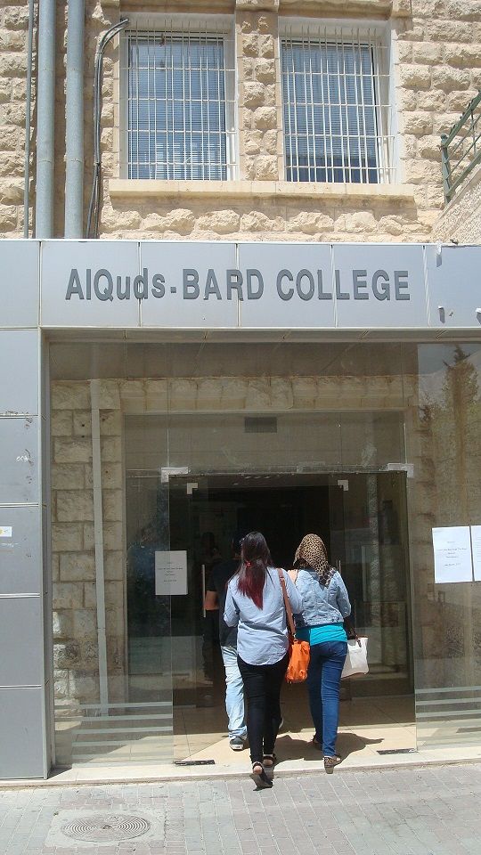 Two people entering a building which reads: AlQuds Bard College