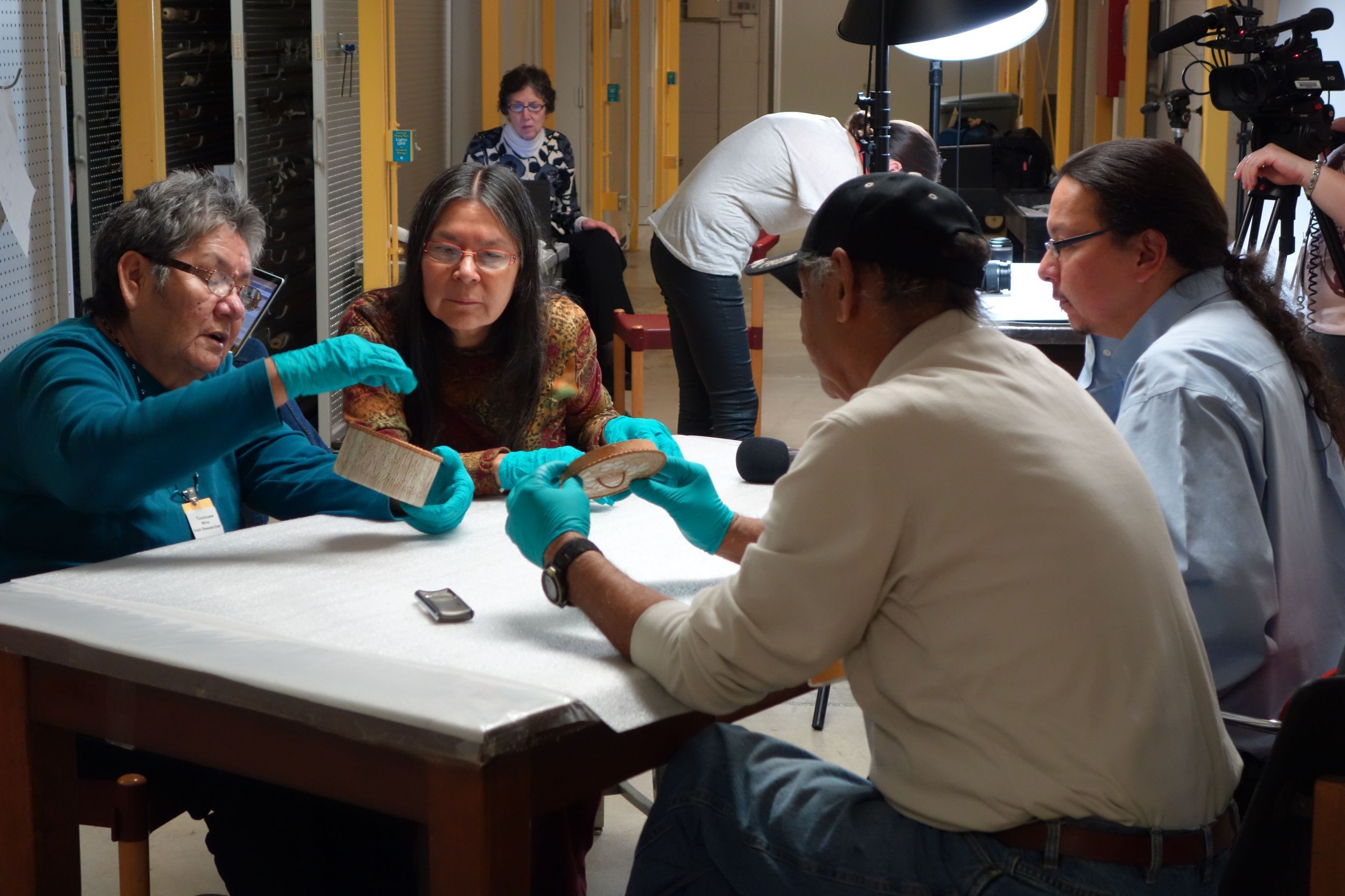 Four people wearing gloves sit at a lab table and study an artifact.