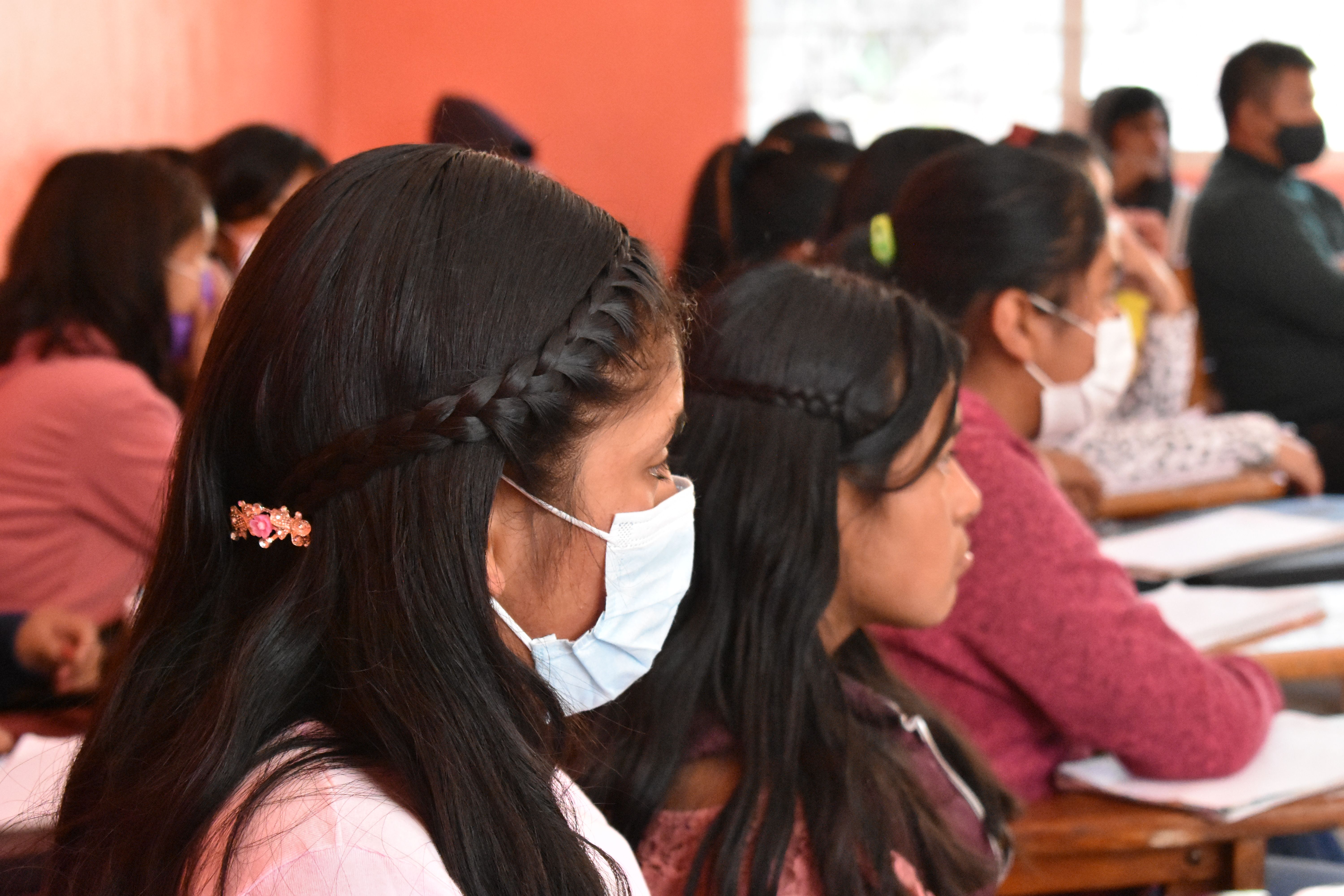 A student sits, wearing a mask, in a row of her classmates
