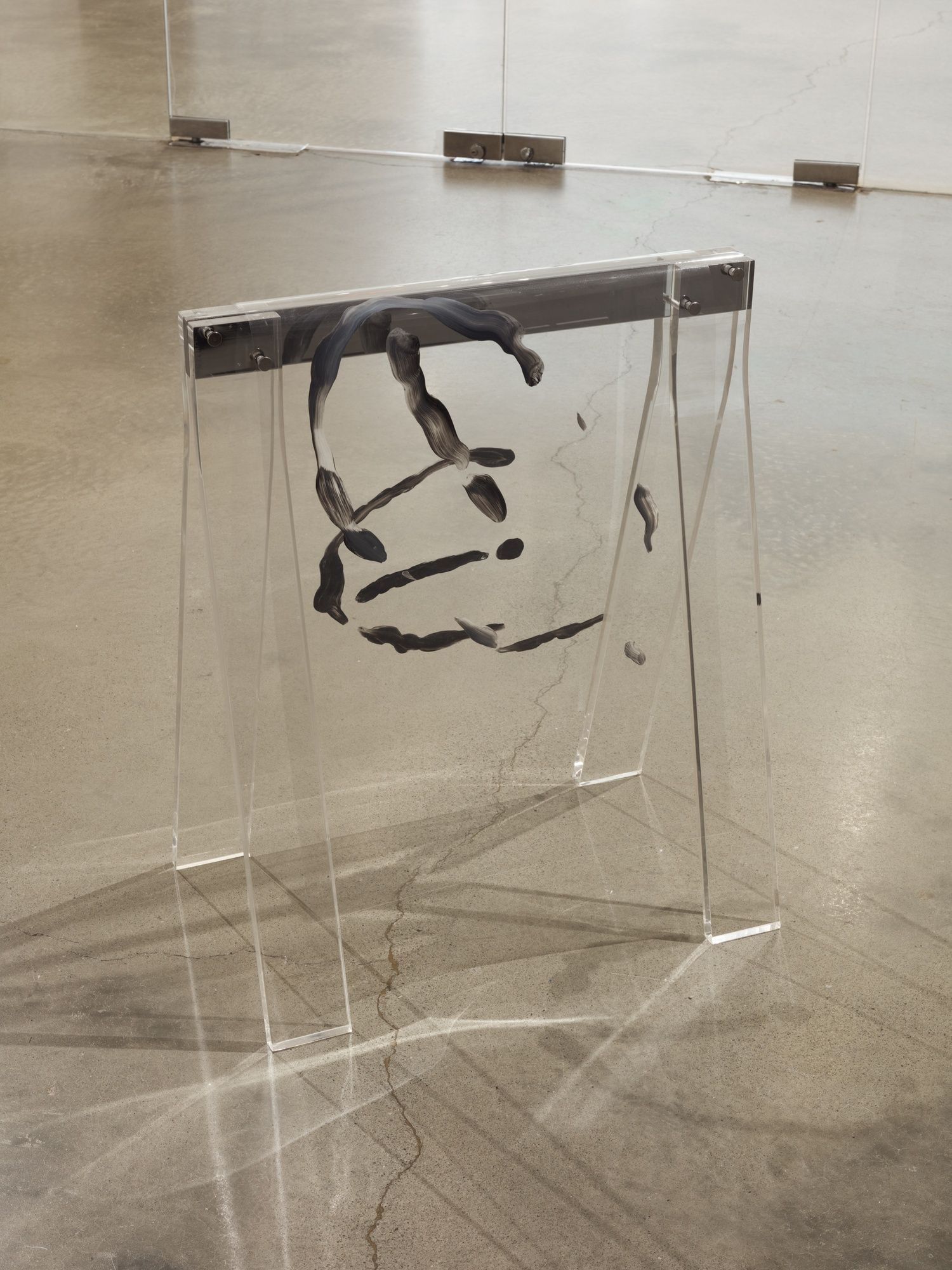Lines of dark gray paint on a clear, plastic sheet with clear plastic legs. It is a sculpture, the paint appearing three dimensional.