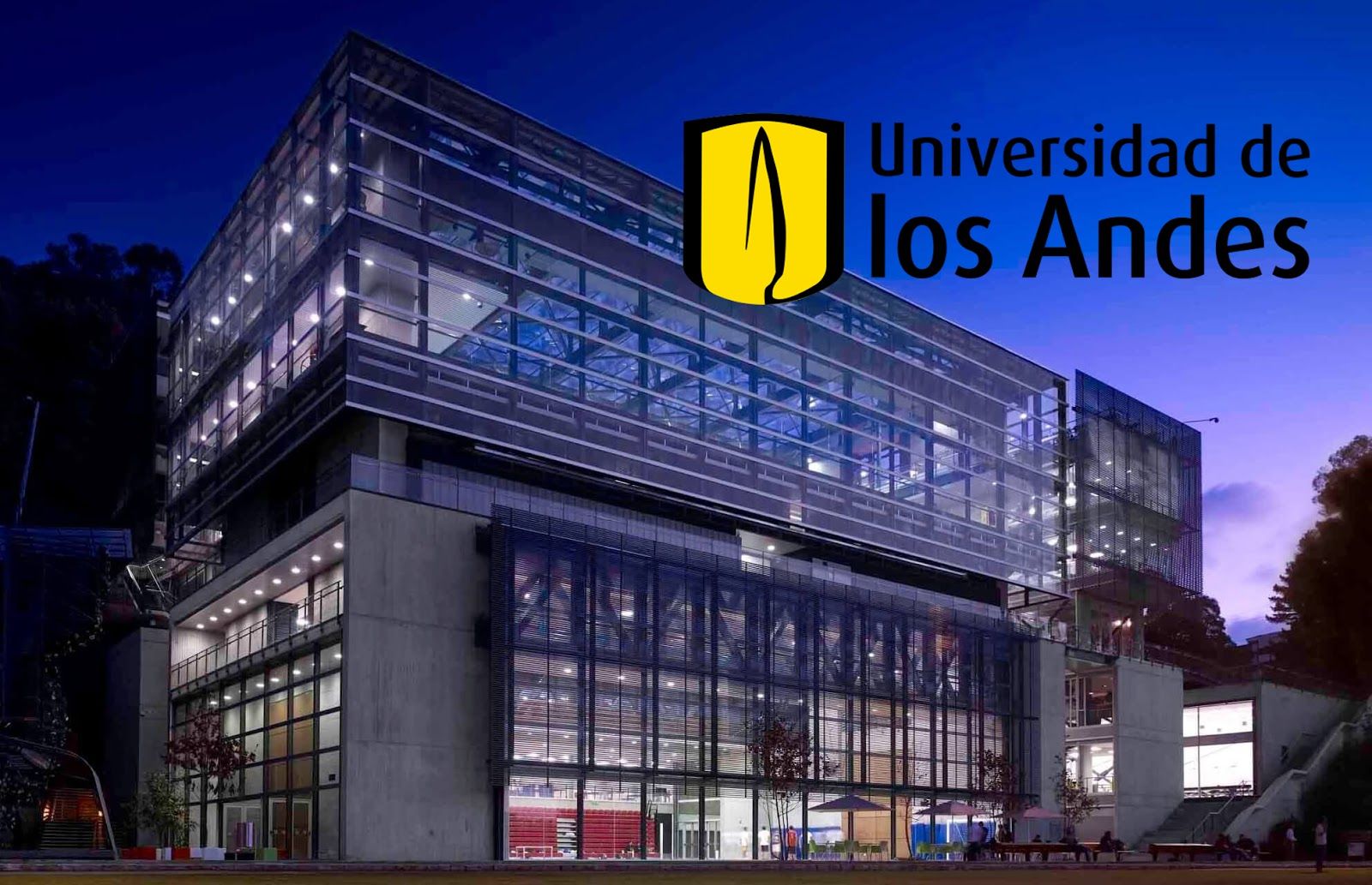 A large glass and cement building at night. Universidad de los Andes logo.