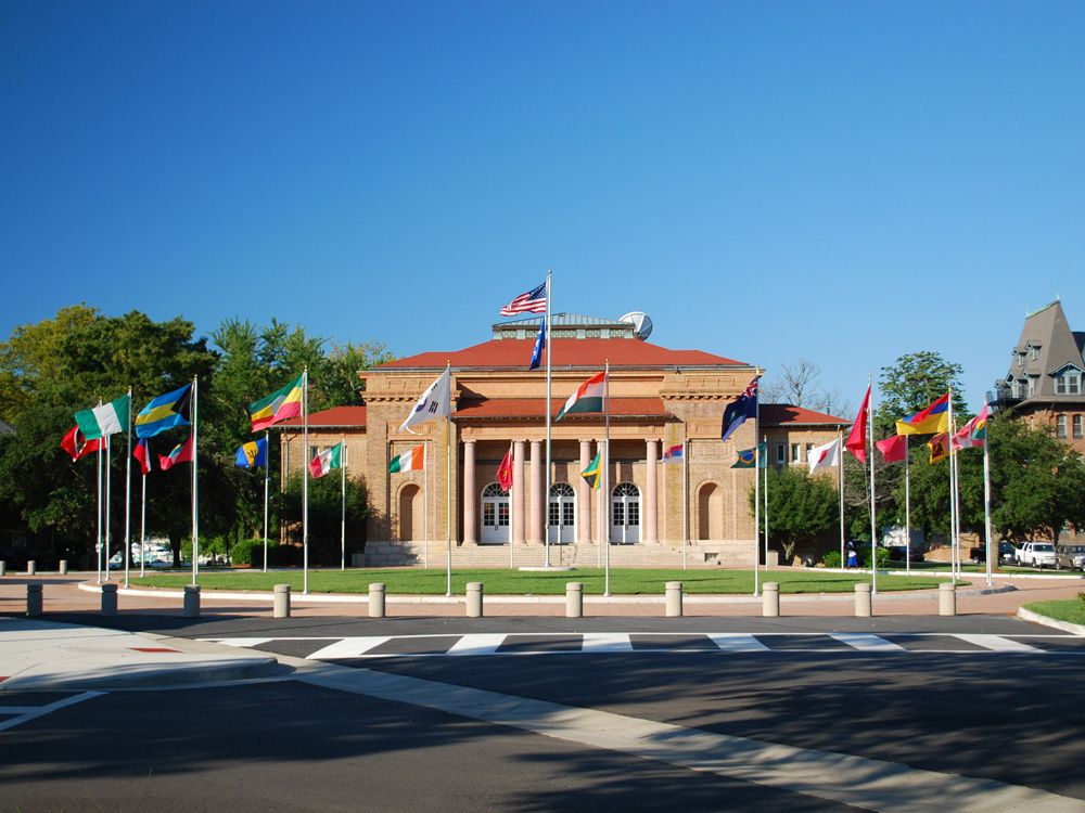 A building with a ring of flags from various countries in front of it, on a circular lawn.