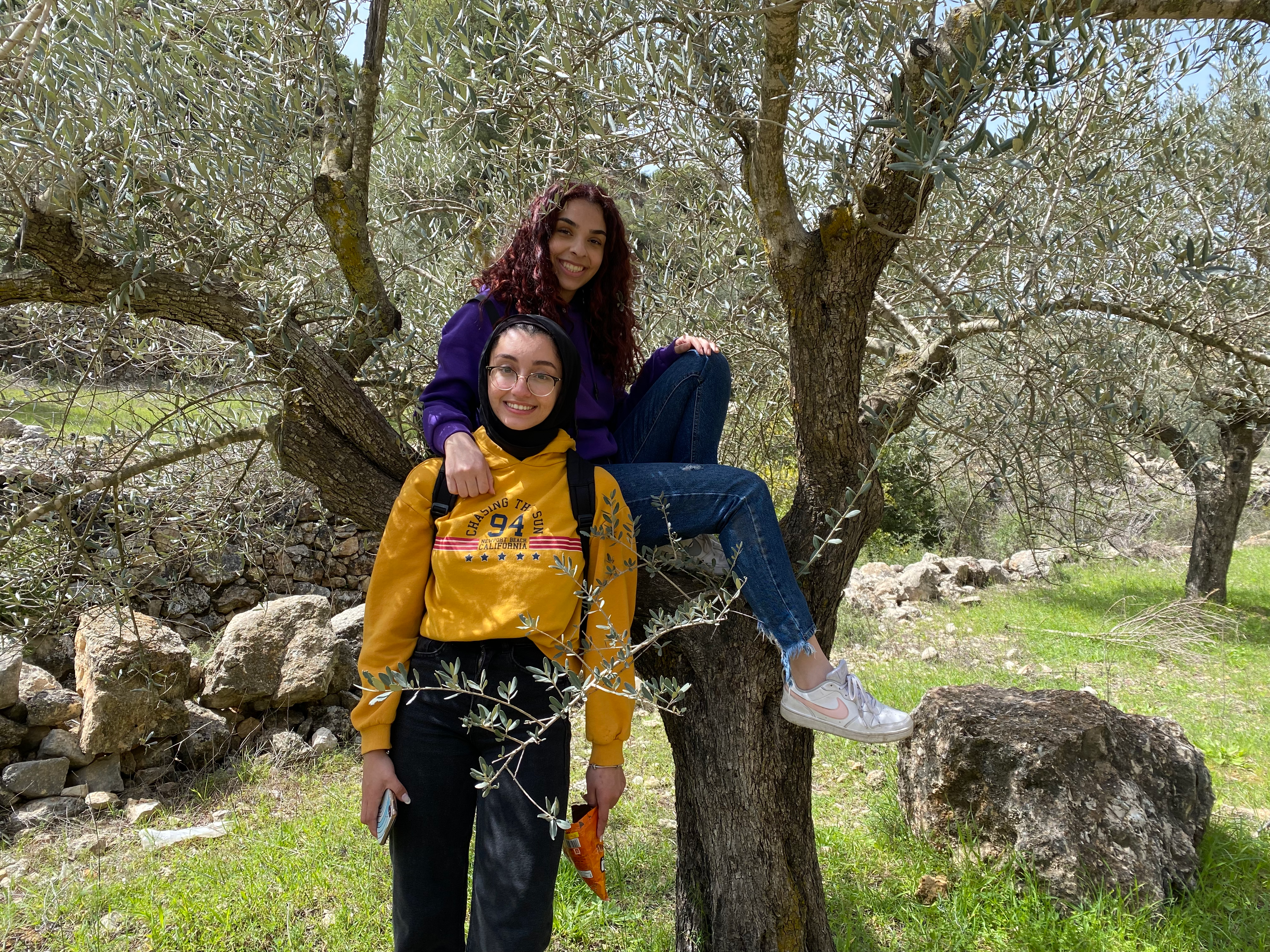Two students smile and pose, one sitting in a tree.