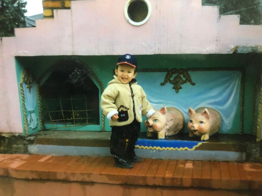A toddler smiling in front of a small outdoor stage with two pig statues on it.