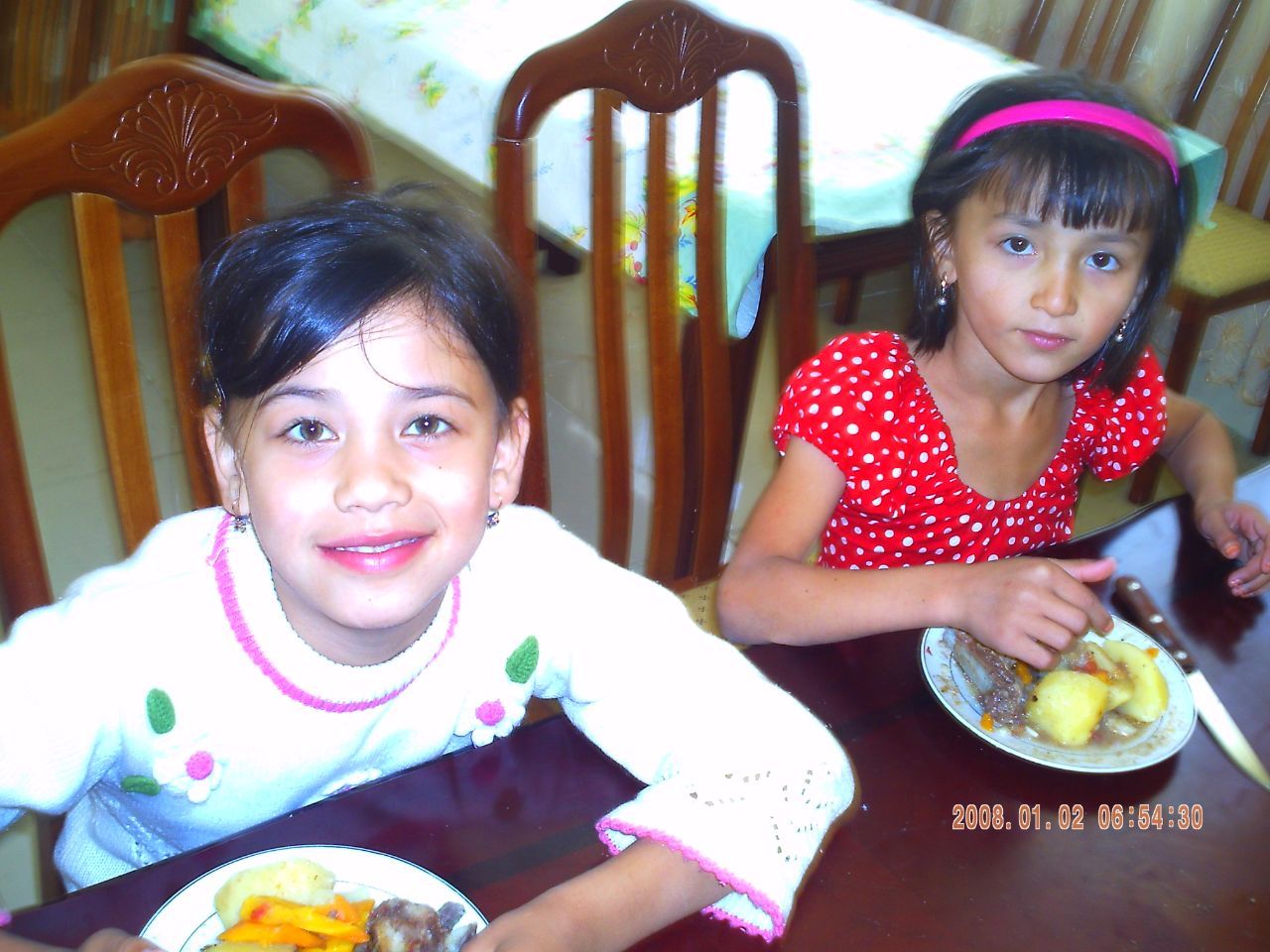 A photo of two girls sitting at a table, over a meal.
