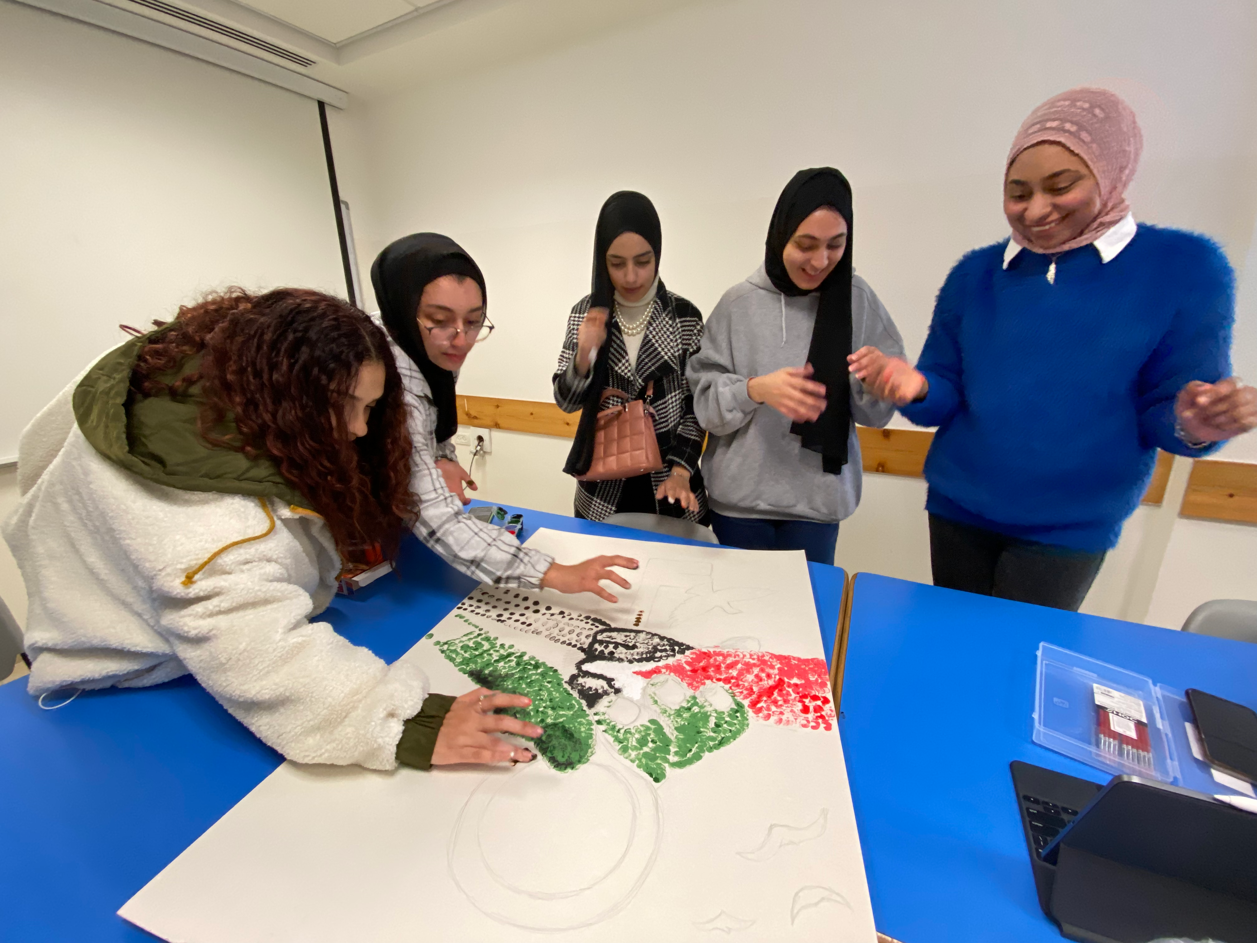 Five students work on a painting composed of many fingerprints, in the colors of the Palestinian flag.
