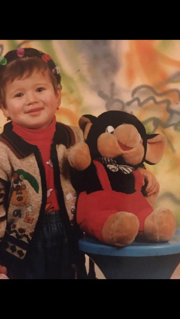 A toddler in a sweater posing with a stuffed elephant.