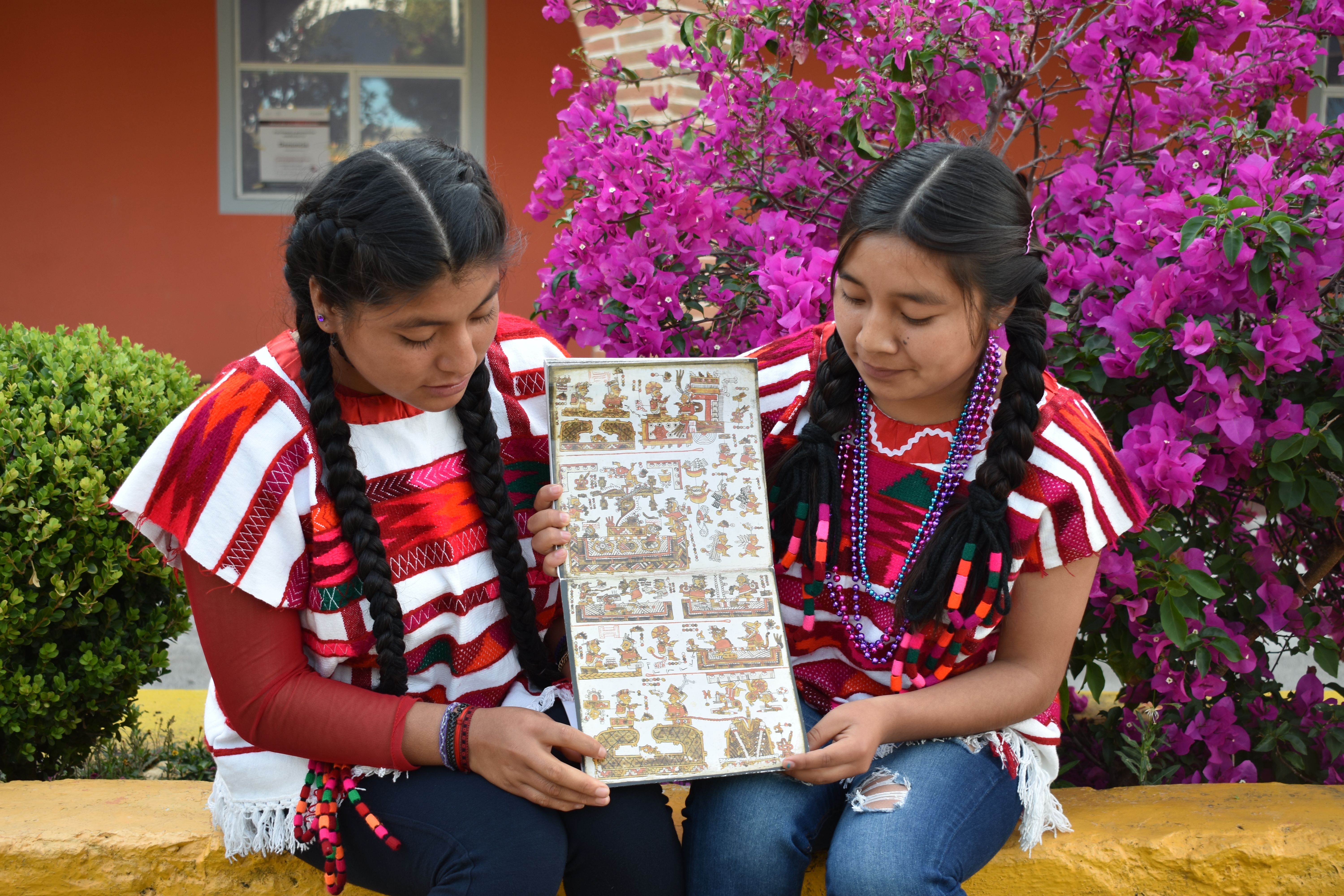 Two girls hold up a codex page