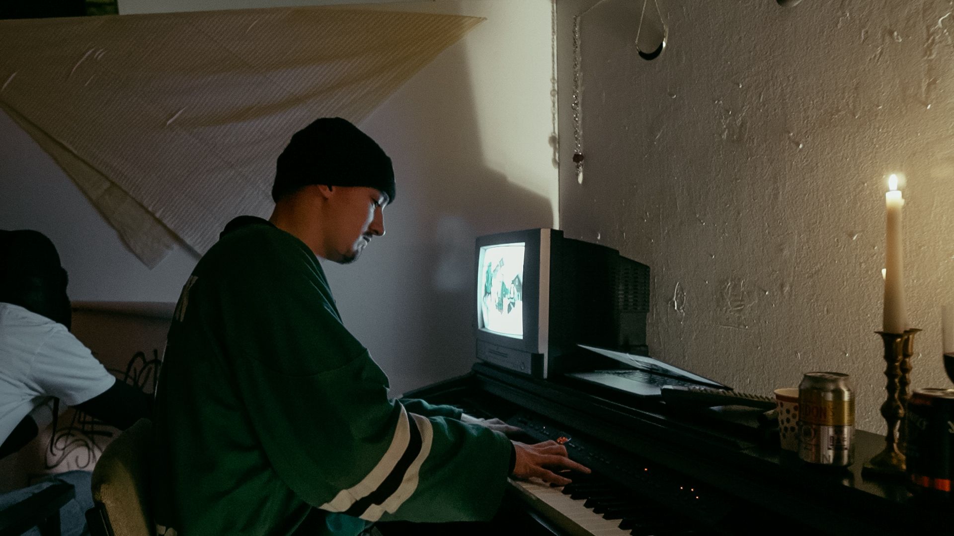 A student plays a piano with a small TV monitor and a lit candlestick on its top