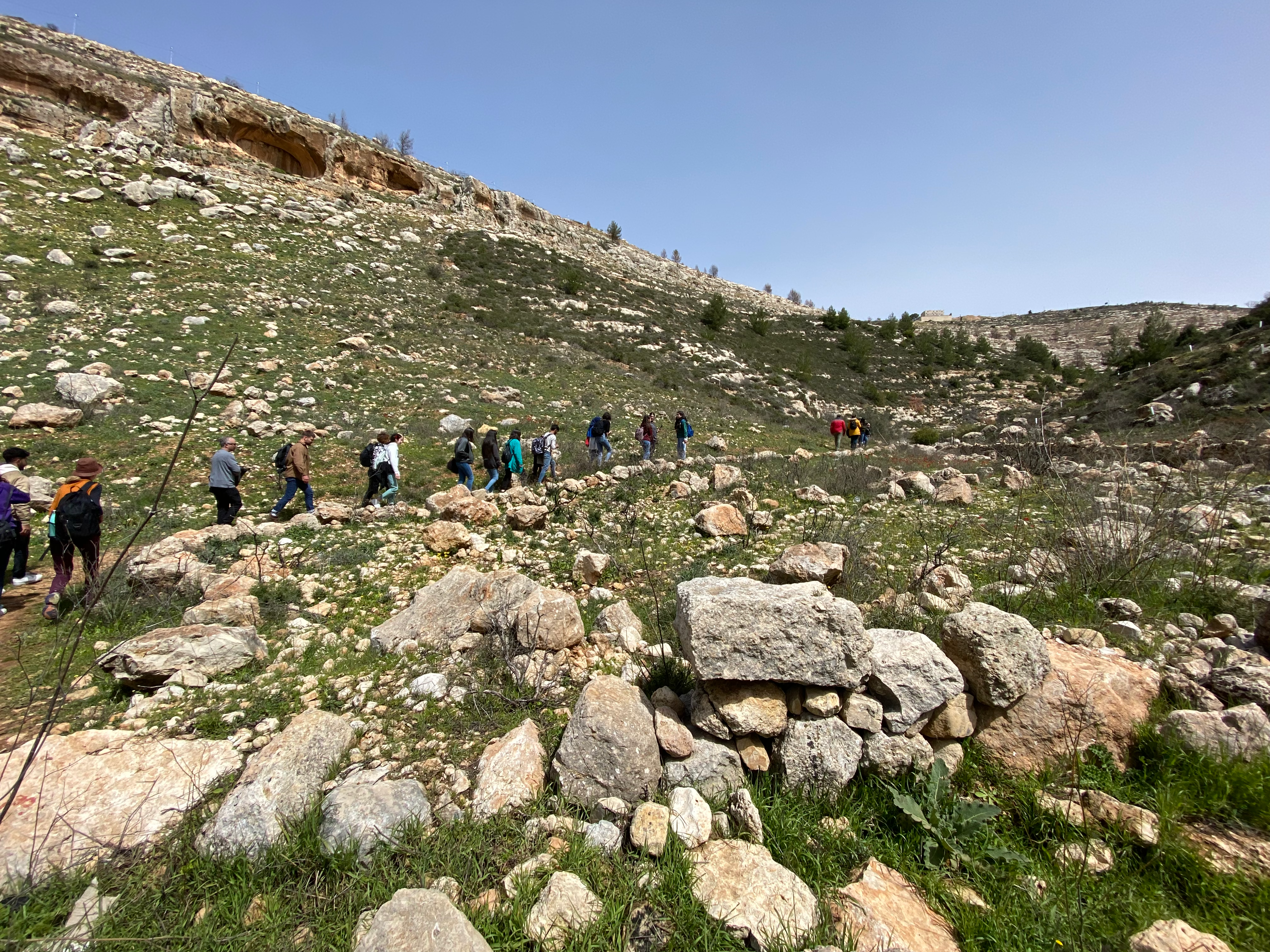 Hikers head up a hill on a trail, single file.