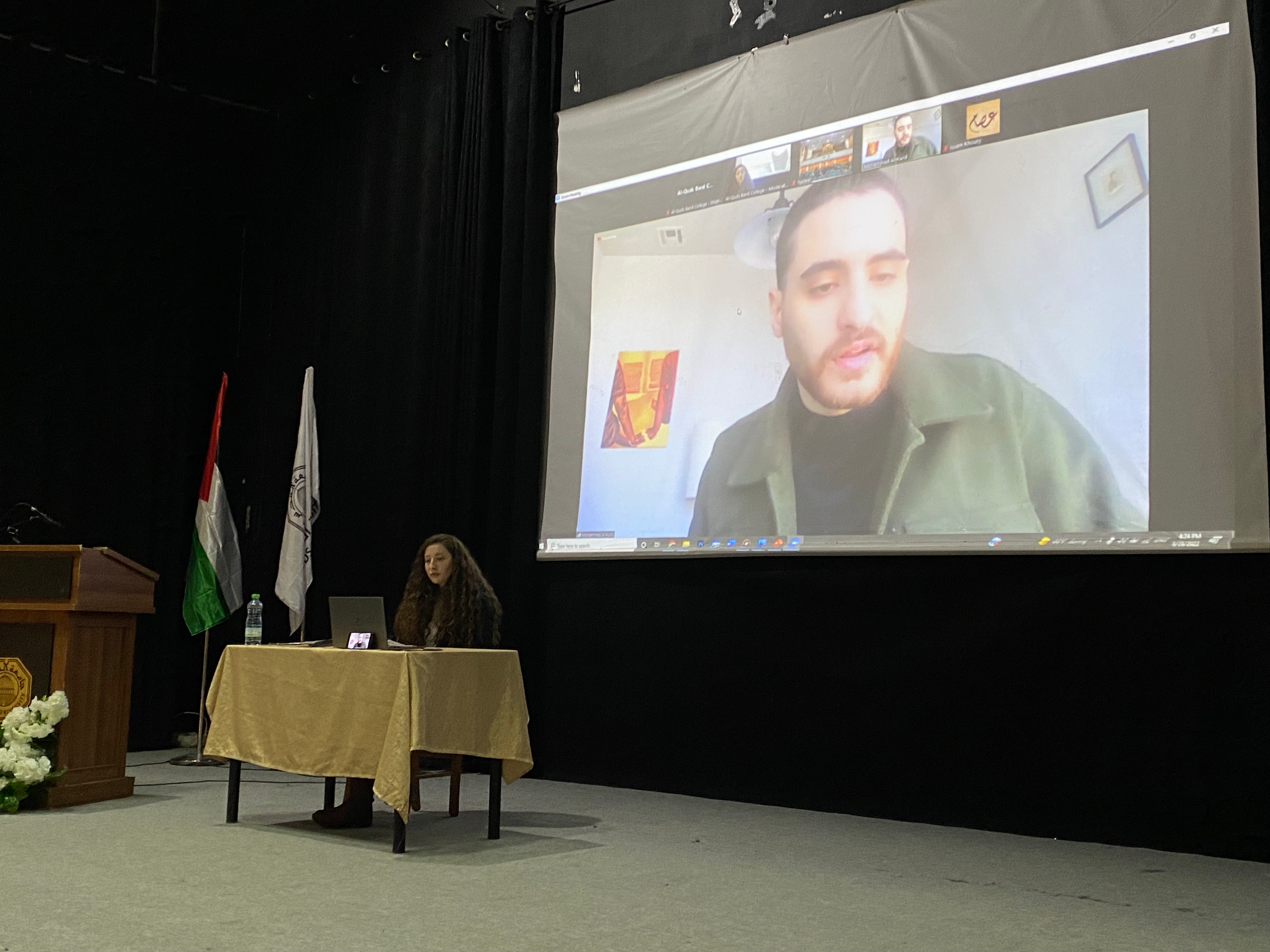 Dalia Alayassa (seated at table) and Mohammad El-Kurd (on Zoom, projected onto a large screen behind Dalia).