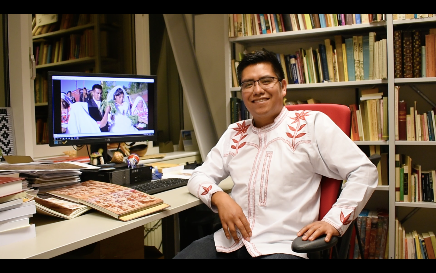 Aguilar poses at an office desk, in front of a computer showing a wedding scene.