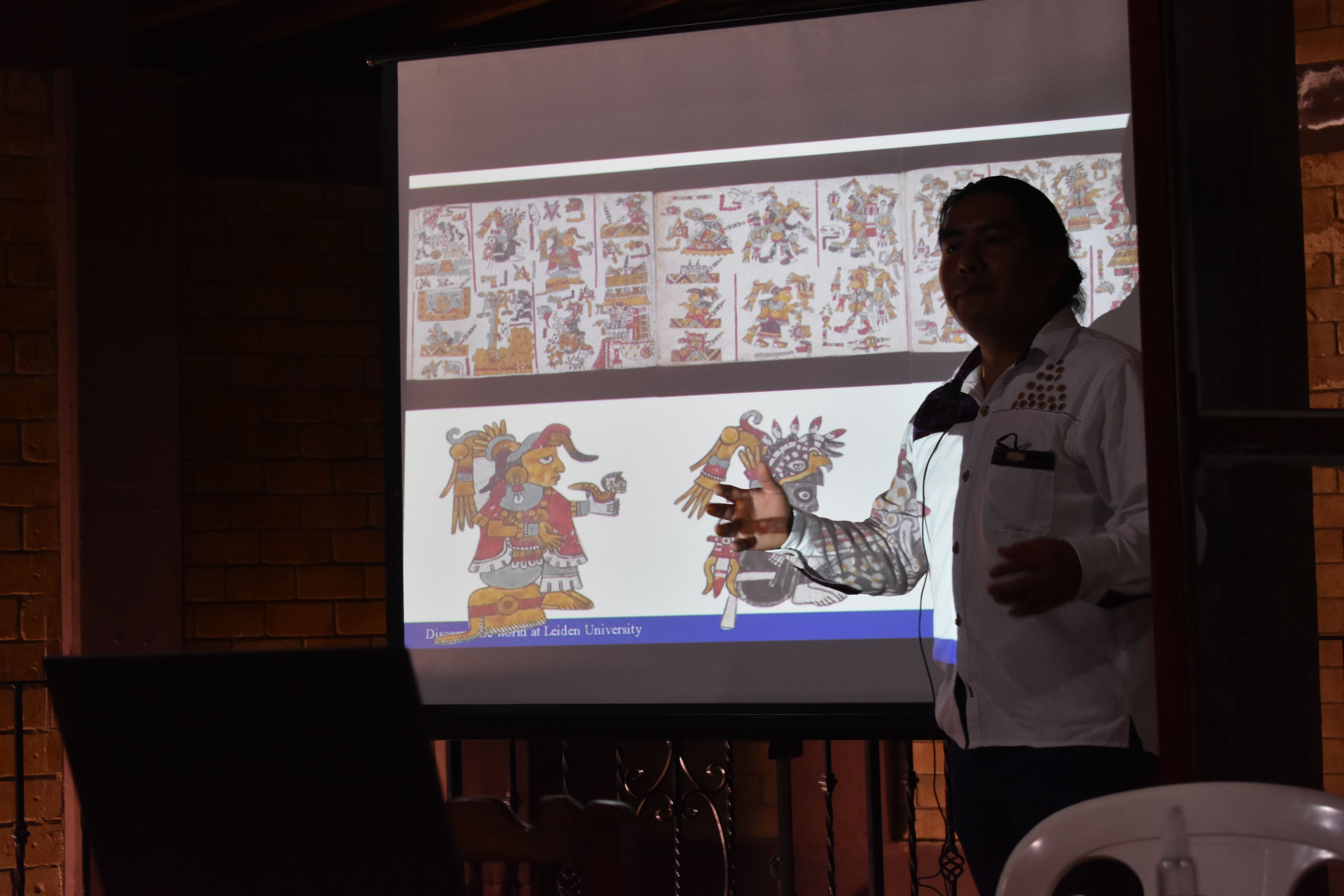 Aguilar presents, standing in front of a codex image projected on a screen
