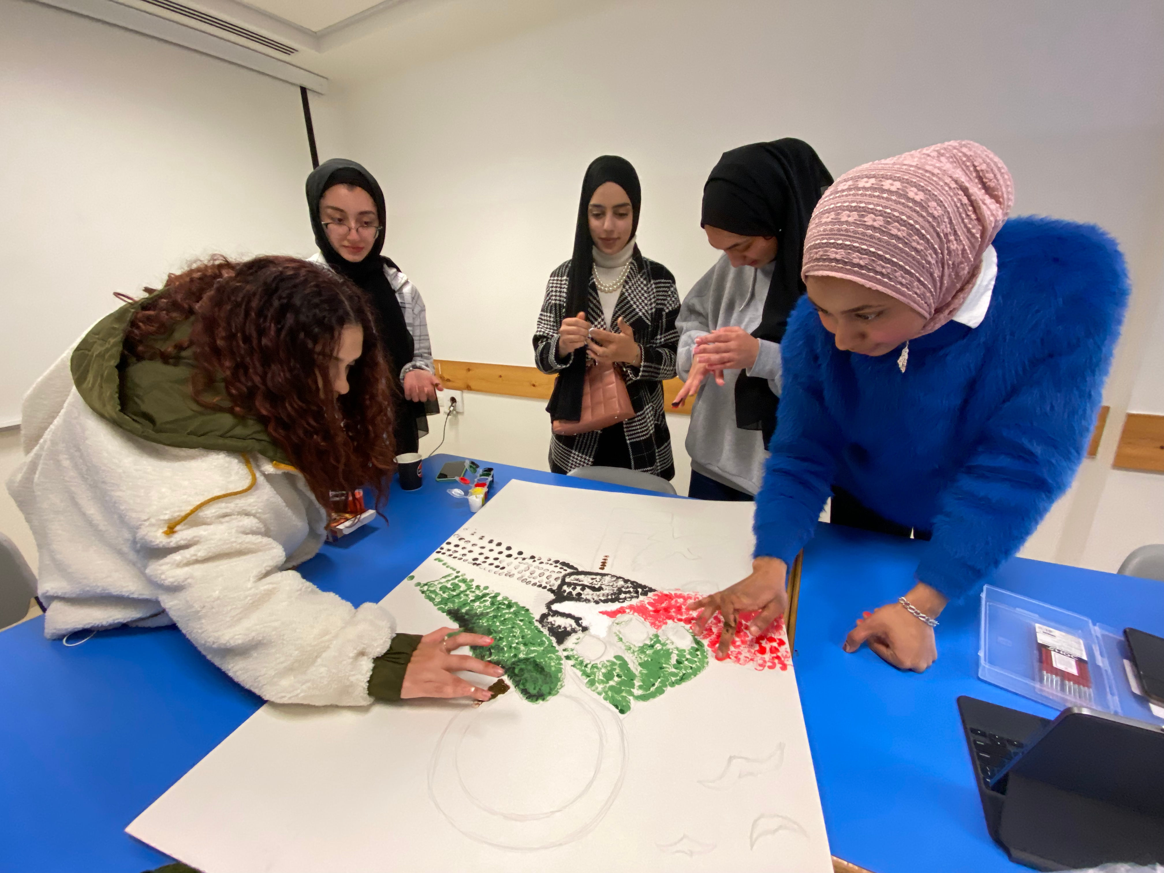 Five students work on a painting composed of many fingerprints, in the colors of the Palestinian flag.