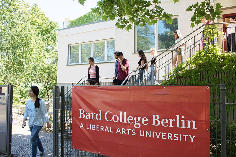 Students walk down the stairs in front of a building. A banner on the gate reads: Bard College Berlin. A liberal arts university.