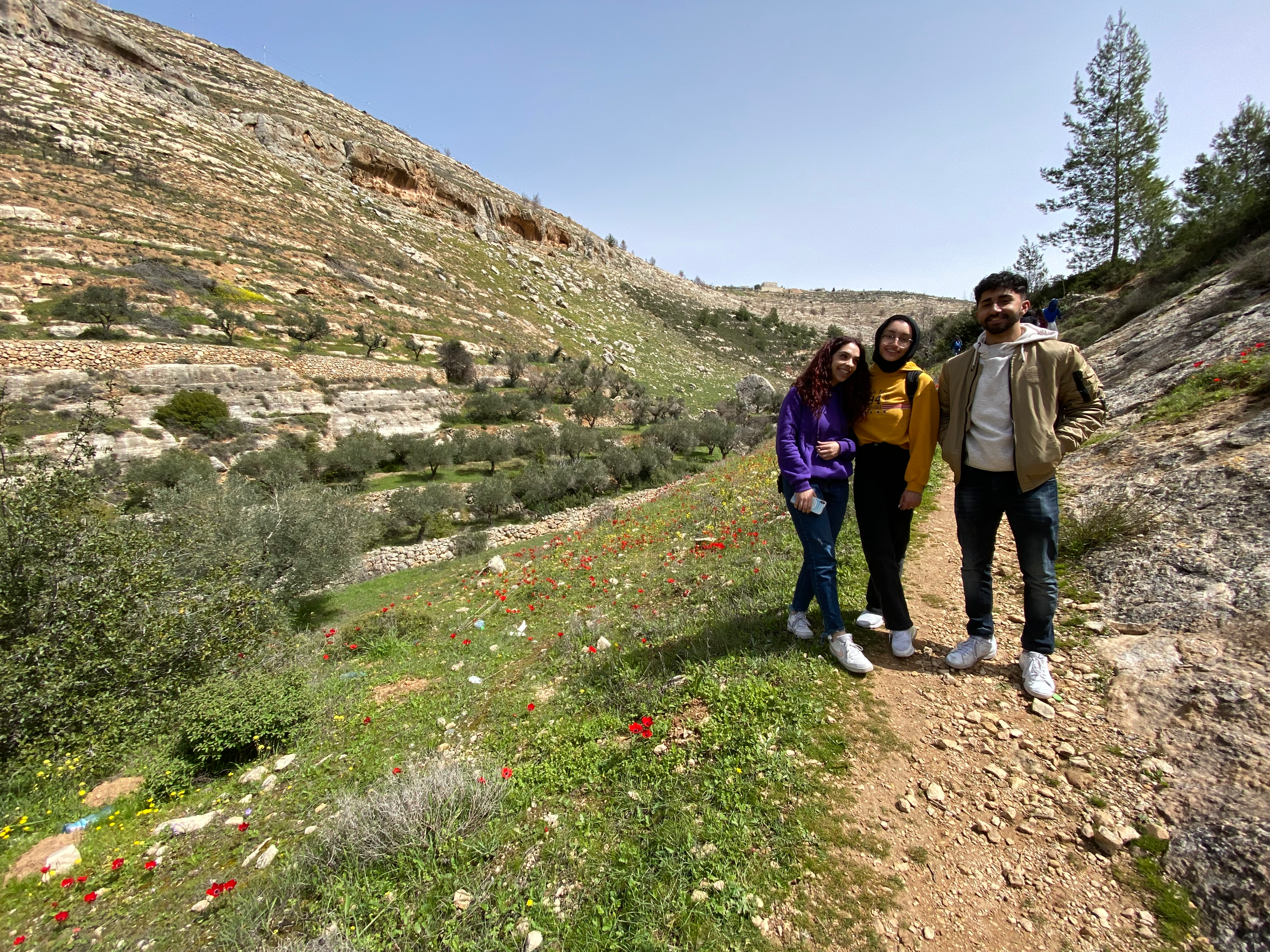 Three students pose on the trail next to a hill.