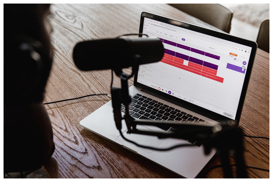 A podcasting mic in front of a laptop with a recording software open.