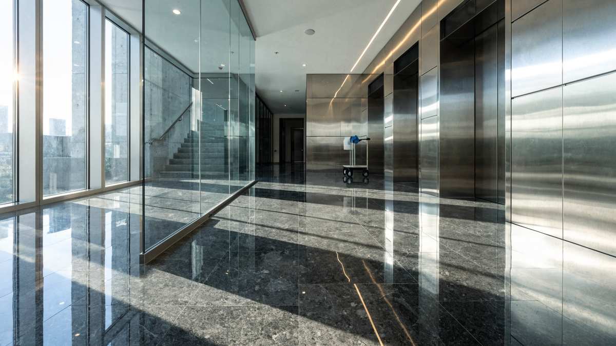 A sleek modern condominium lobby with polished stone floors and a cleaning cart near the elevators.