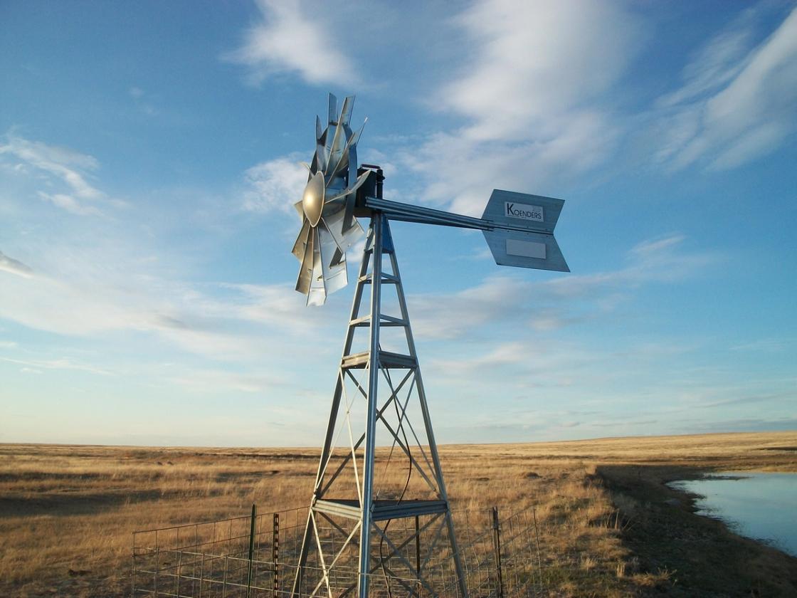 A branded Koenders wind-powered aeration system beside a farm dugout on the open prairie