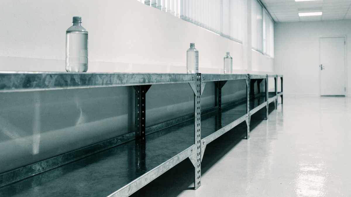 A nearly empty supply shelf holding just three cleaning bottles spaced neatly apart in a bright storeroom.