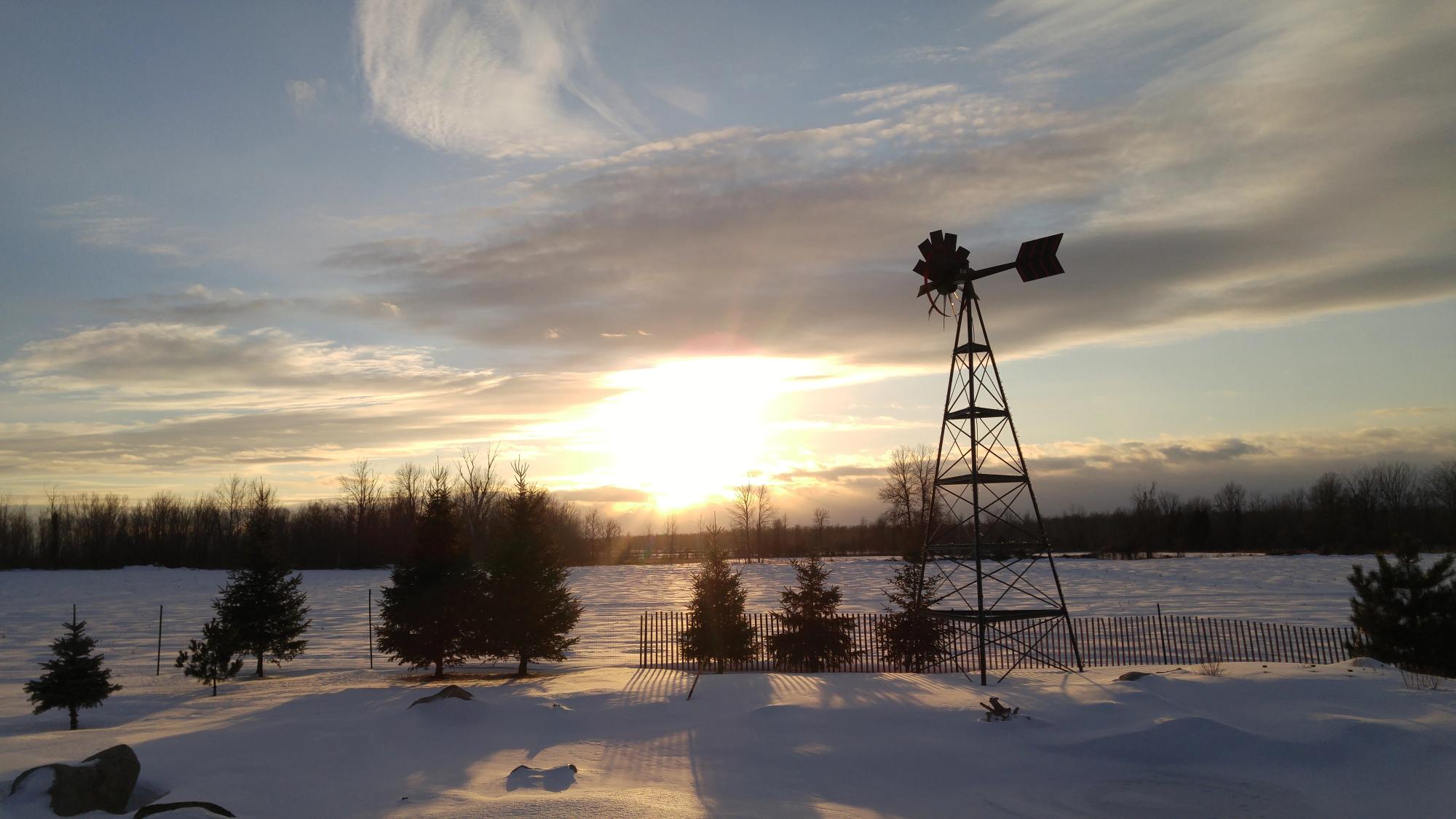 A Koenders aeration windmill silhouetted against a winter sunset over a snowy prairie field