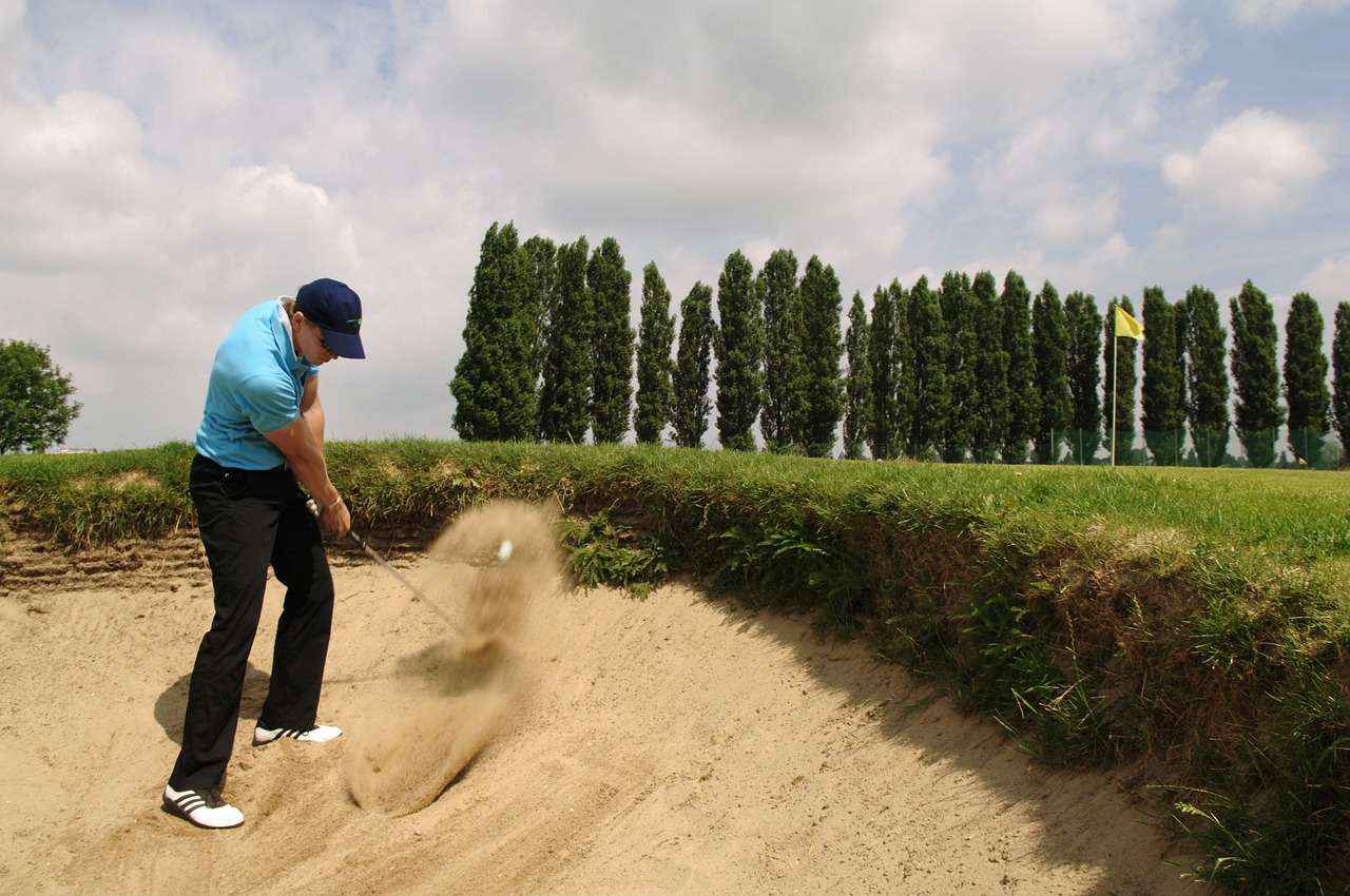 un golfista che esce da un bunker: che ne diresti di una lezione di golf per completare i servizi per una vacanza di lusso?