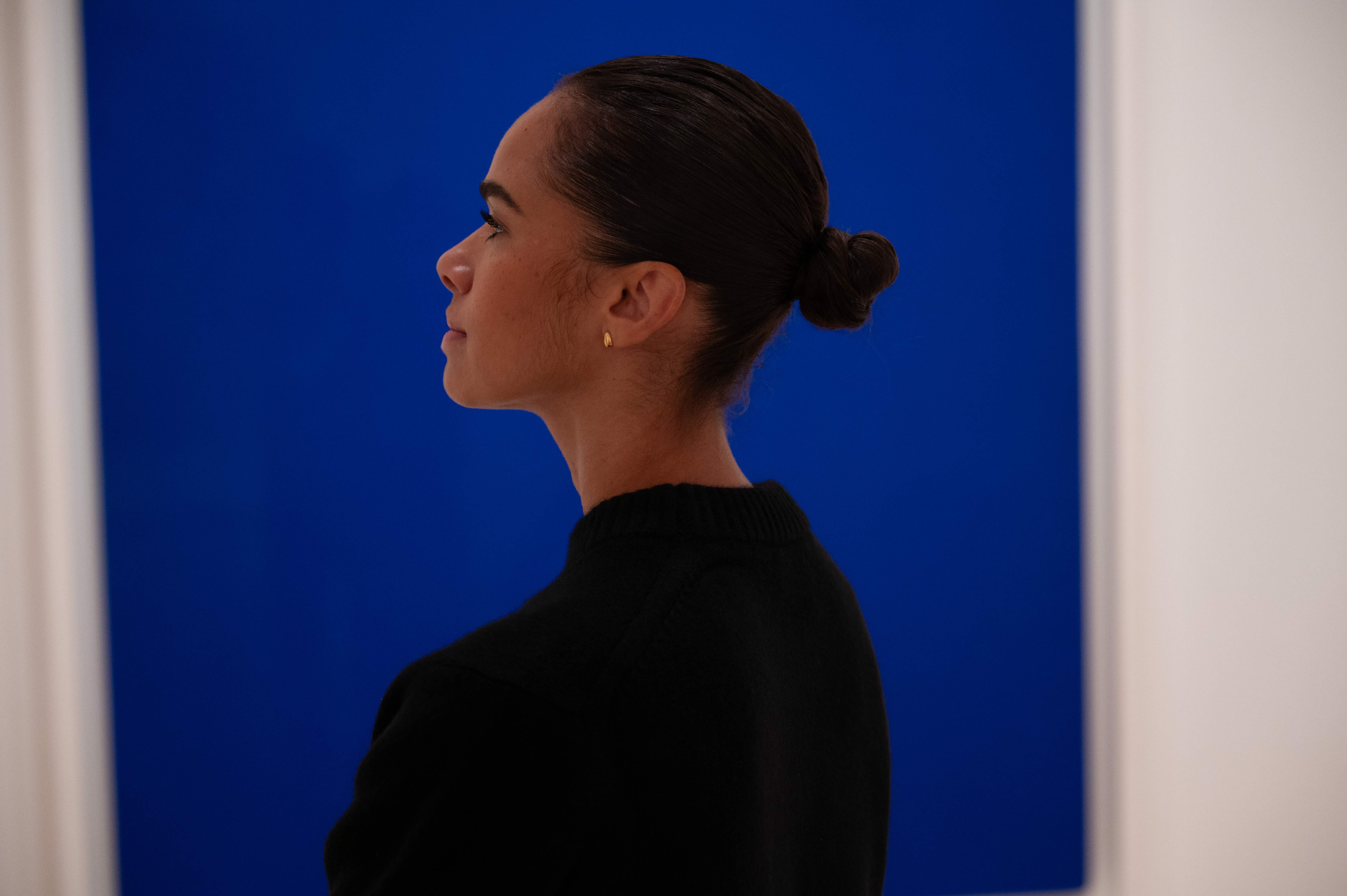 Profile view of a person standing in front of a blue painting. 